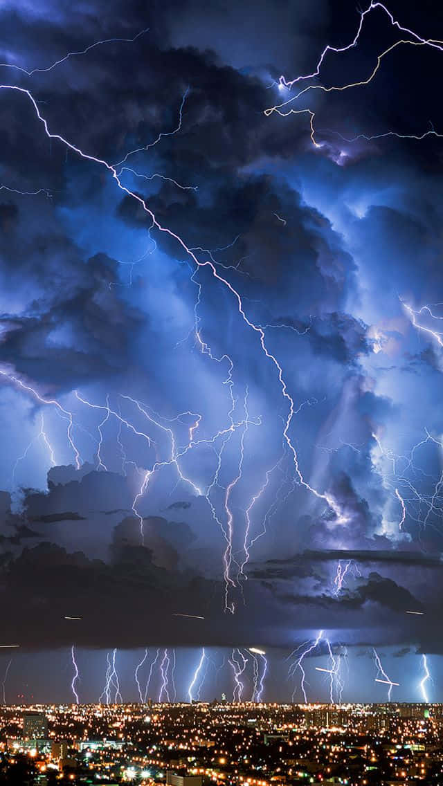 Lightning iPhone 桌布 壁紙 — 強烈的閃電在暴風雨的夜空中劃過，下方是燈火輝煌的廣闊城市景觀。