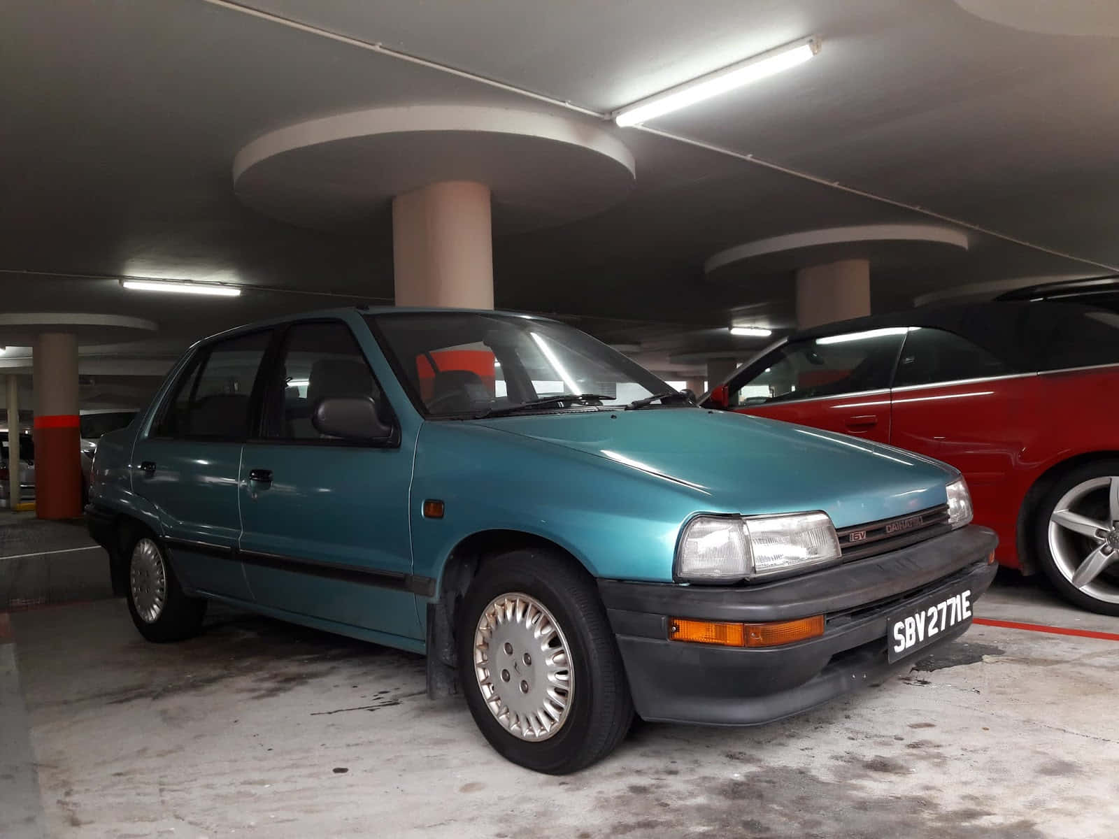 Daihatsu Charade 桌布 壁紙 — 一輛青綠色復古掀背車停放在光線昏暗的多層混凝土停車場，頭頂有螢光燈。
