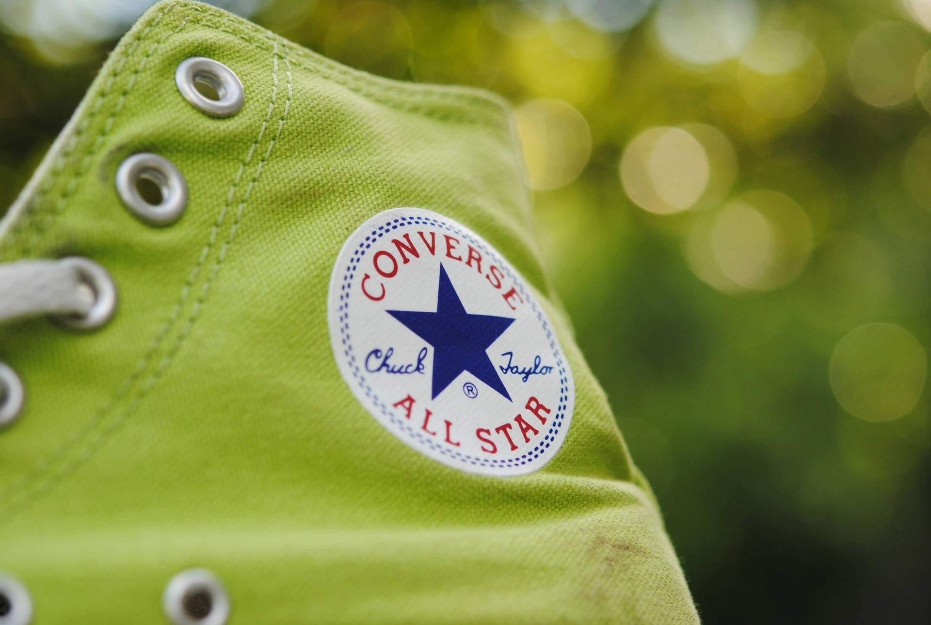 檸檬綠 Converse 壁紙 — 青檸綠色Converse Chuck Taylor All Star運動鞋特寫，配有白色鞋帶和銀色鞋眼，背景為模糊的綠色散景。