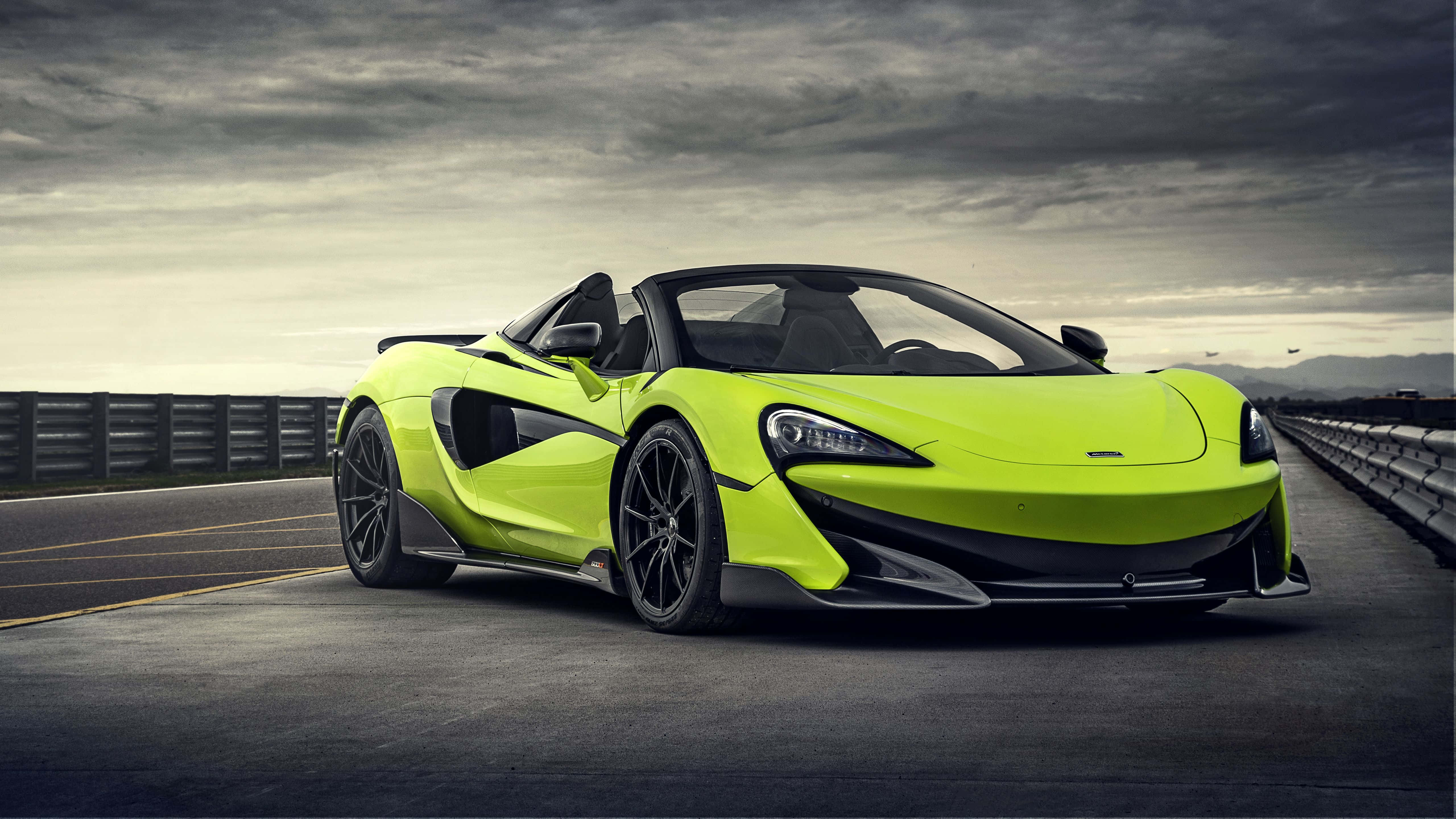 Mclaren 600lt 桌布 壁紙 — 一輛鮮豔的青檸綠色McLaren 570S Spider跑車停泊在陰沉多雲的天空下的高速公路上。