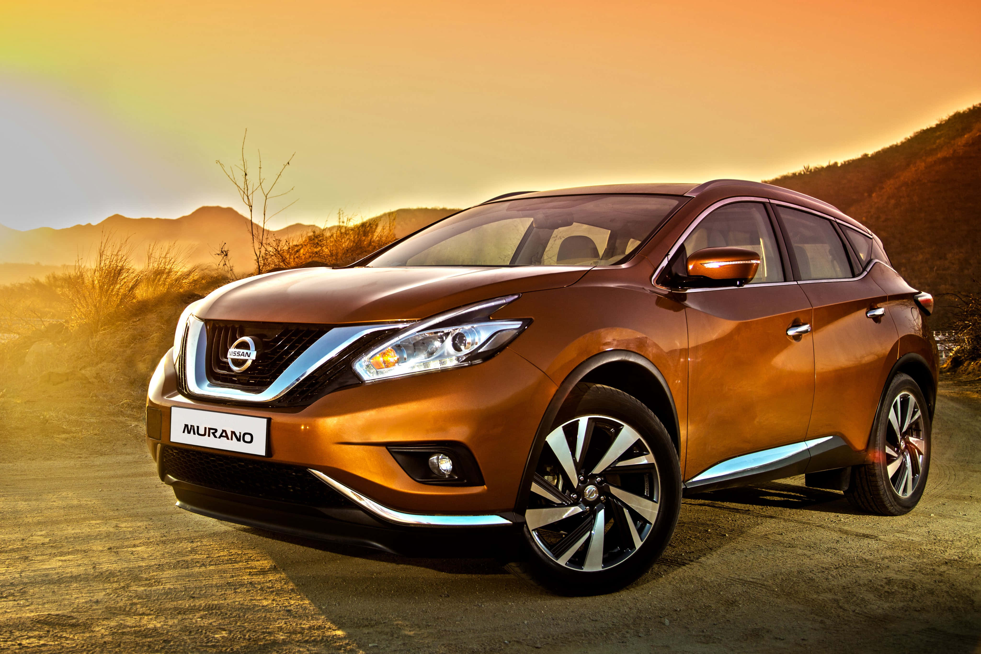 Nissan Murano 桌布 壁紙 — 一輛青銅色的日產Murano SUV在溫暖的夕陽下閃耀，遠處山丘上有一道淡淡的彩虹。
