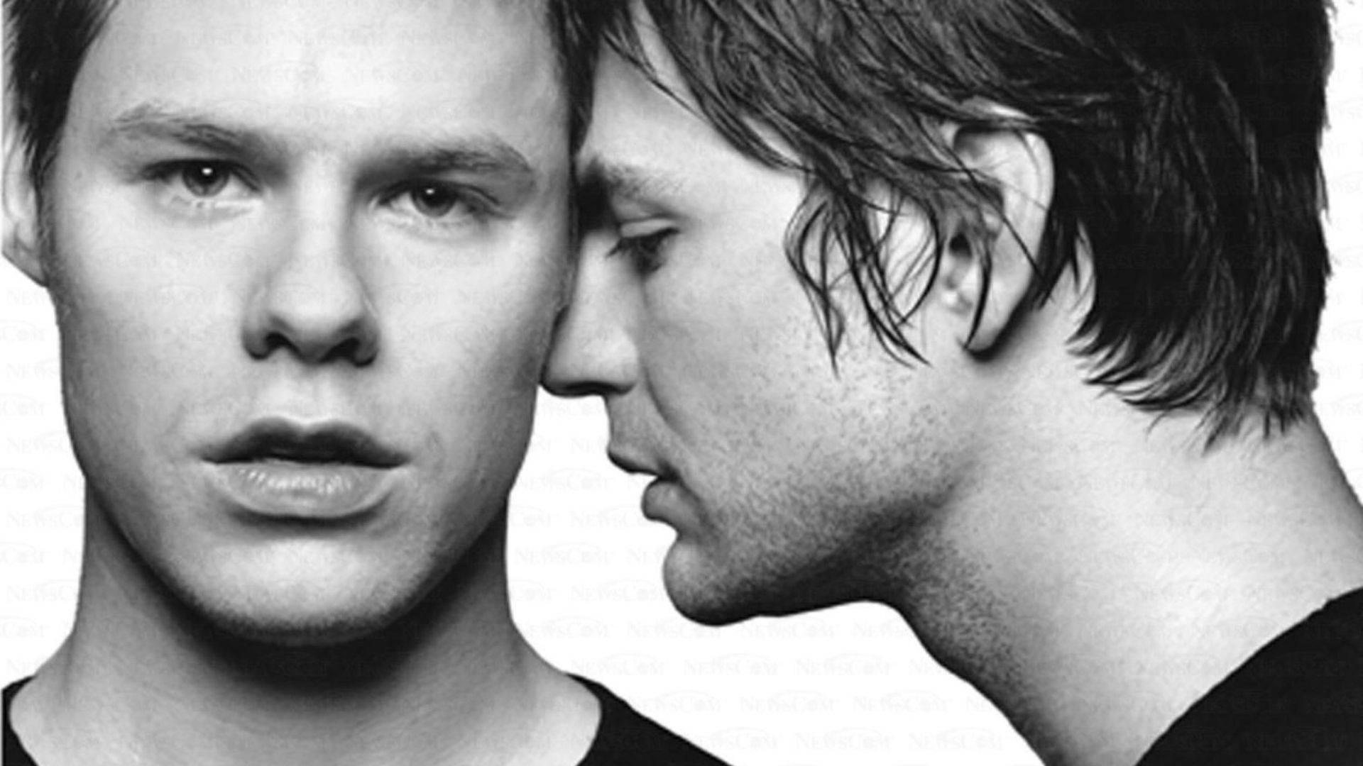 《Queer As Folk》主角們的親密時刻 壁紙 — 兩個黑白人像的男子親密地面對面，一個正面一個側面，背景簡潔。