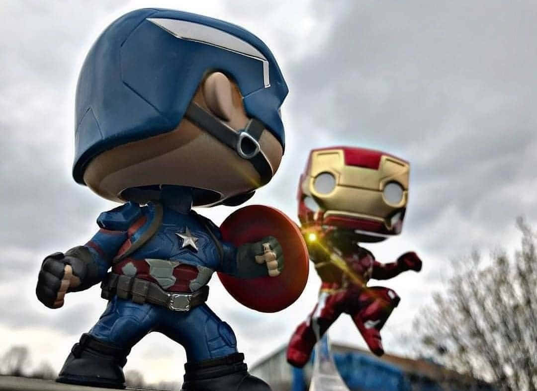 Iron Man Pop Figures 桌布 壁紙 — Q版美國隊長和鋼鐵俠人偶在陰天背景下，以英雄姿態擺出姿勢，背景有光禿的樹木。