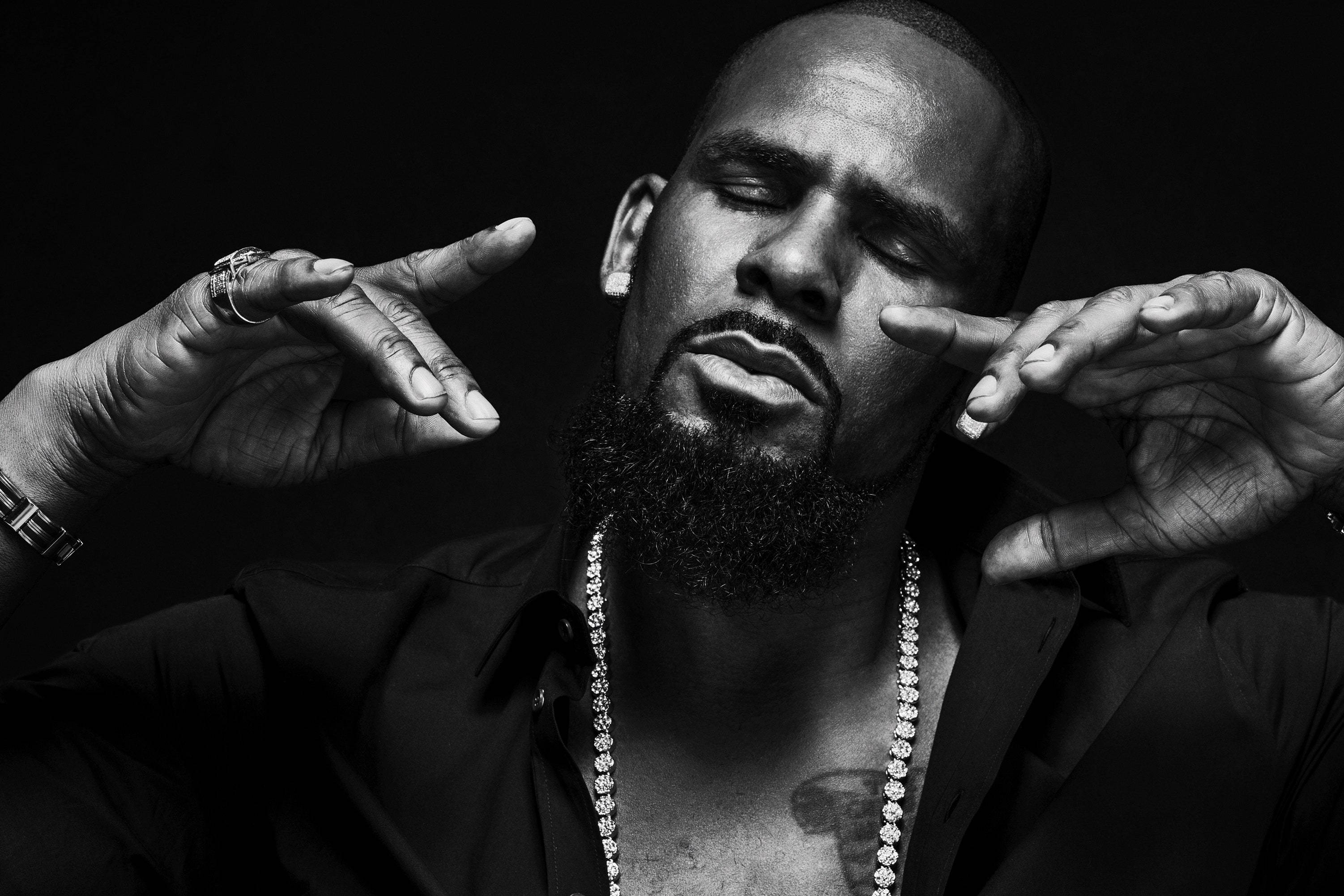 R. Kelly 黑白工作室肖像 壁紙 — 一個留鬍鬚的男人戴著鏈條和戒指，在臉旁做手勢的黑白肖像。