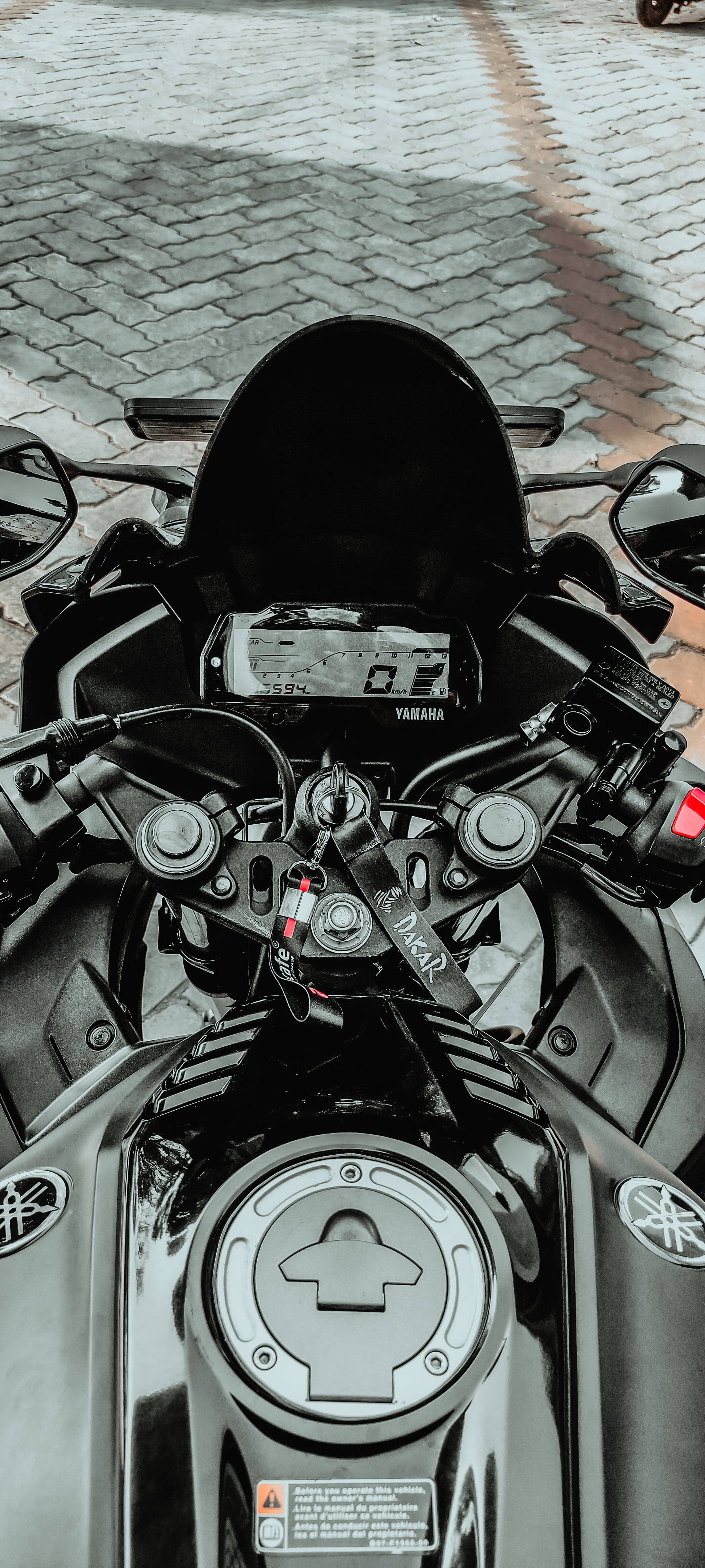 R15 V3 車頂視角 壁紙 — 黑色Yamaha電單車的把手和油箱在鵝卵石街道上的特寫。