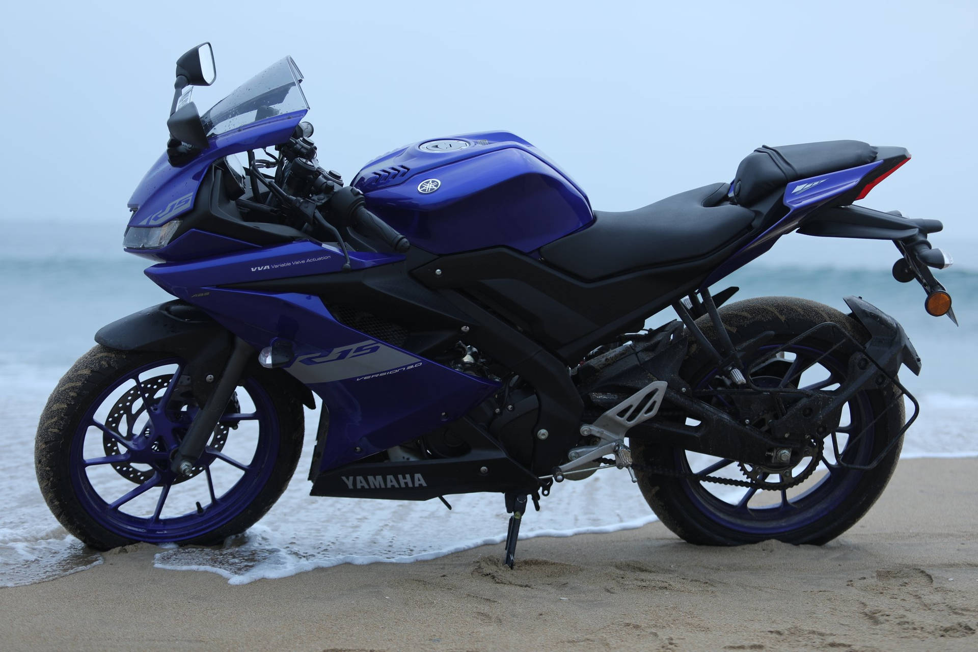 藍色Yamaha R15電單車停泊在海灘上，伴隨海浪