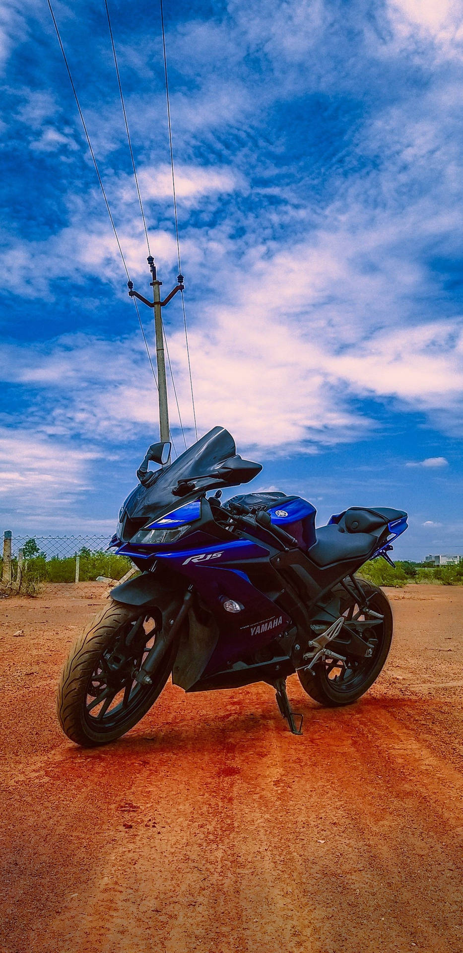 藍色Yamaha R15電單車停在泥路上，背景是晴朗的藍天和白雲。