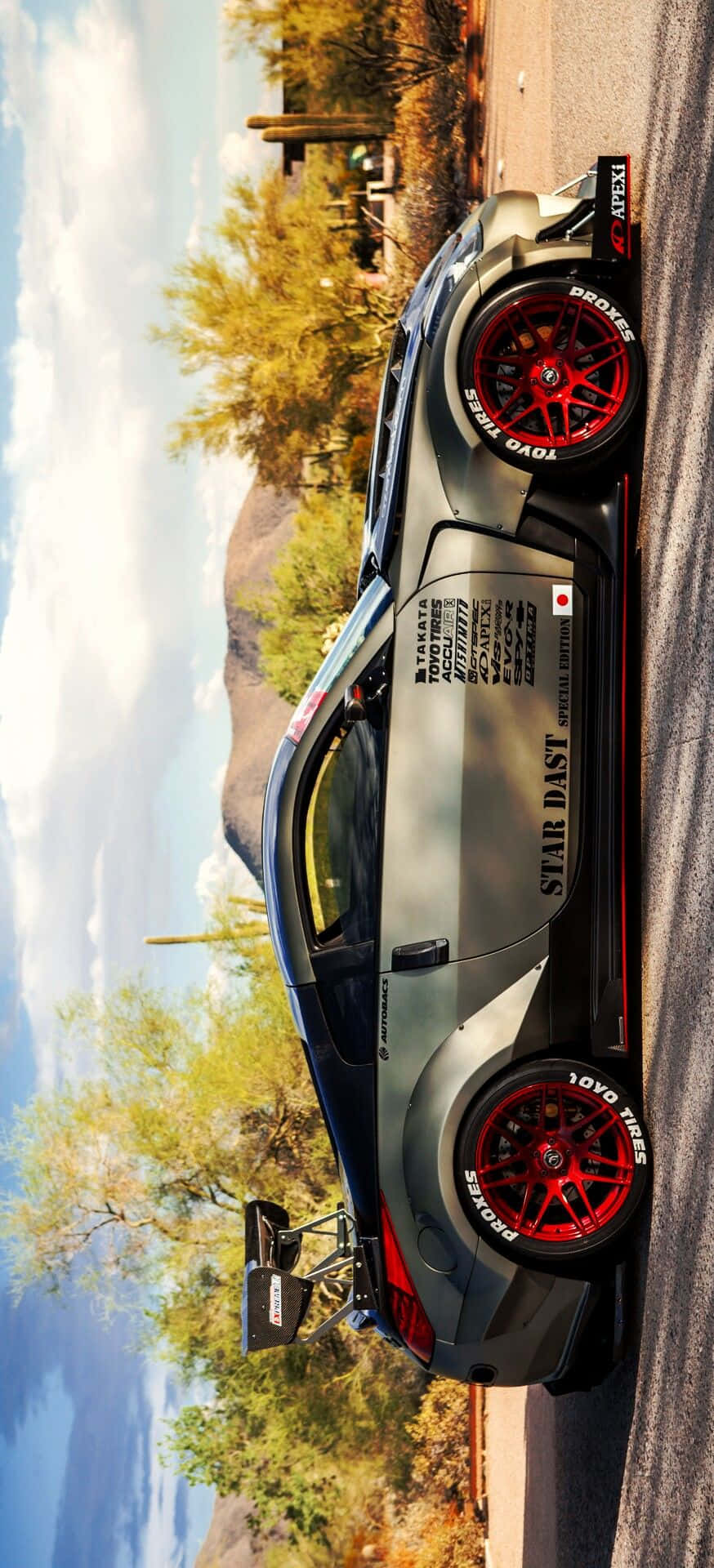 運動感十足的尼桑R35 GT-R 壁紙 — 一架時尚灰色賽車配紅色輪胎，停泊在沙漠公路旁，旁邊有仙人掌和山脈，天空局部多雲。