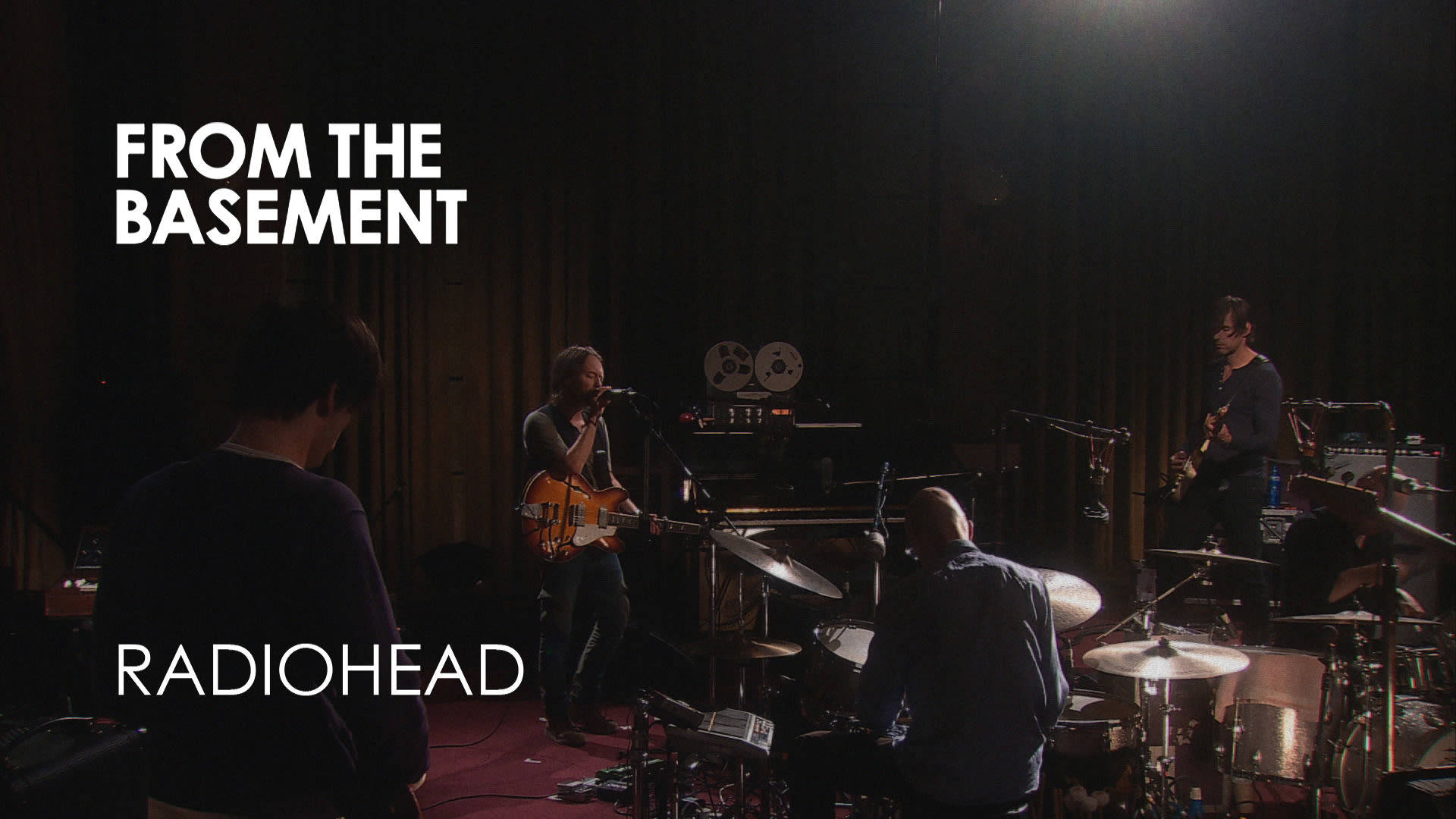 Radiohead 在黑暗的地下場地中進行現場表演，配有舞台燈光。