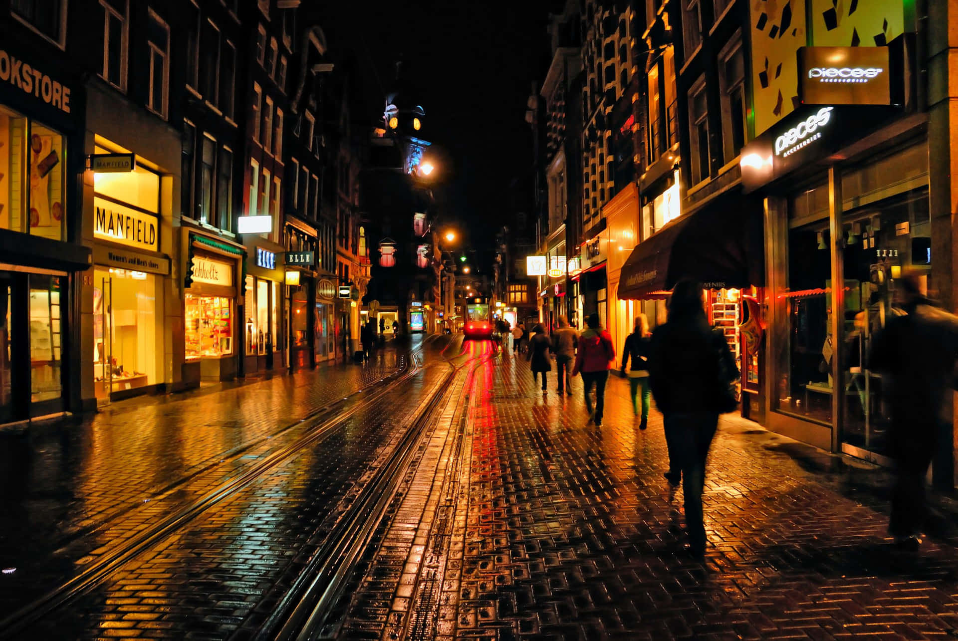 夜晚的城市街道，濕漉漉的鵝卵石反射著商店燈光和模糊的行人。