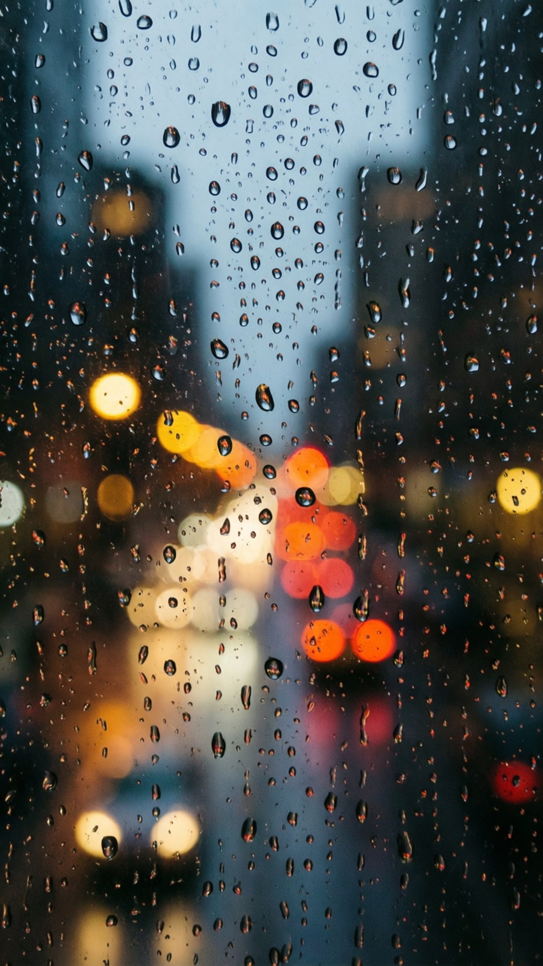 玻璃上的雨滴，模糊的城市燈光在夜間發出橙色和黃色的光芒