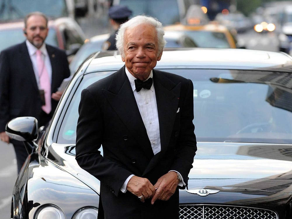 Ralph Lauren 經典賓利造型 壁紙 — 一位身穿燕尾服的年長紳士自信地微笑，站在繁忙的城市街道上一輛時尚的黑色賓利旁邊。