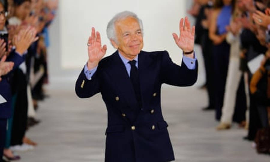 Ralph Lauren 伸展台後秀 壁紙 — 一位身穿海軍藍雙排扣西裝的長者在跑道上熱情地向鼓掌的人群揮手。