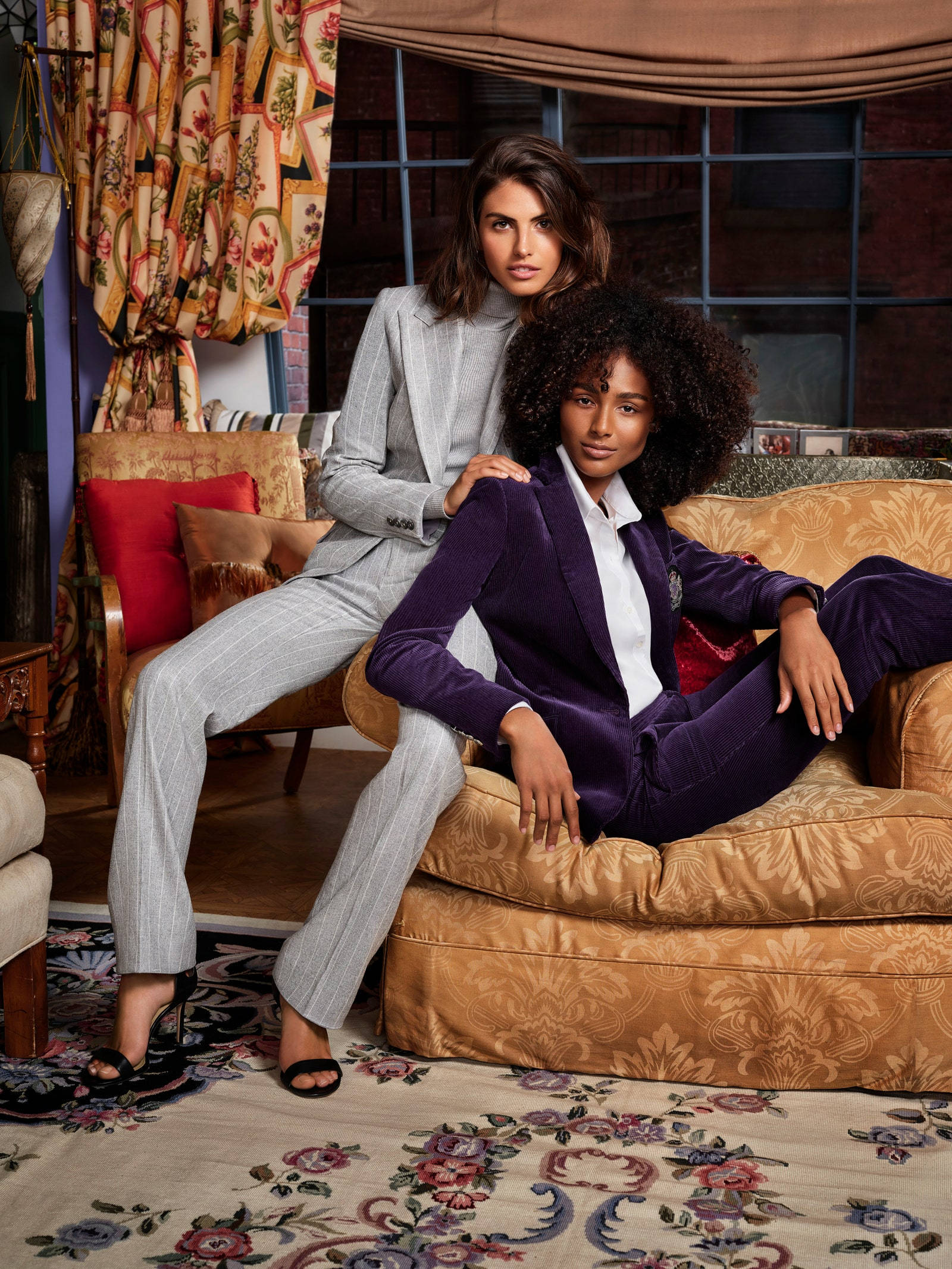 Ralph Lauren 女性力量 壁紙 — 兩位時尚女性自信地擺姿勢，坐在裝飾華麗的復古客廳中的華麗家具上。