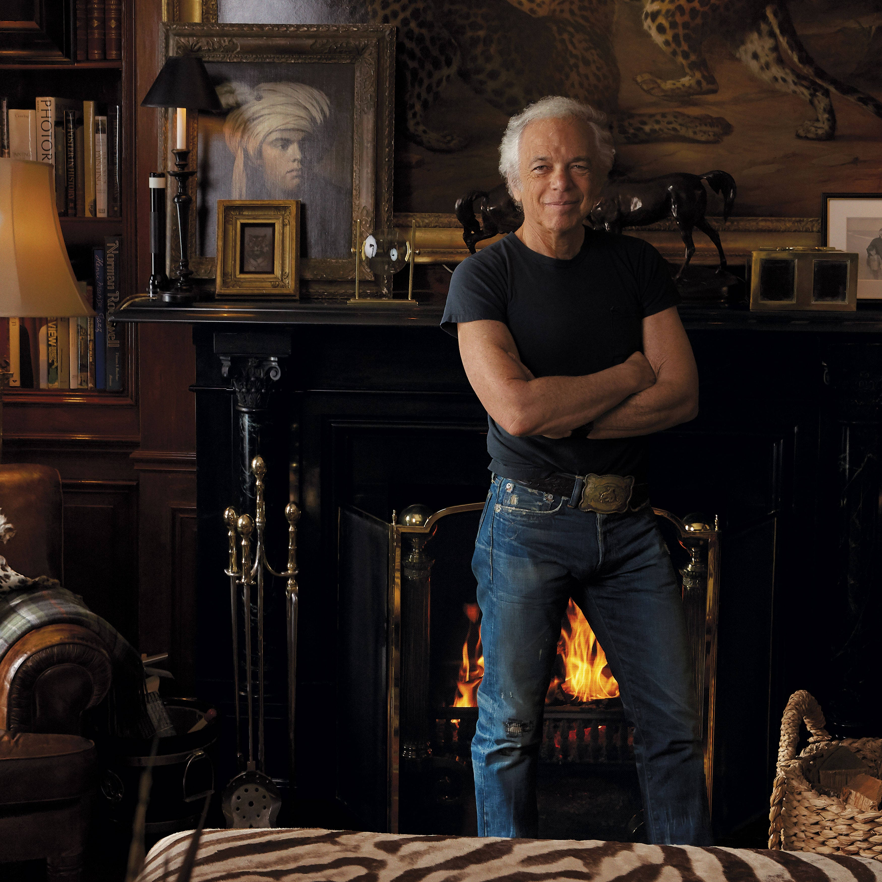 Ralph Lauren 家居 壁紙 — 一個穿著牛仔褲的男人自信地交叉雙臂，站在一個裝飾華麗的書房裡咆哮的壁爐前。