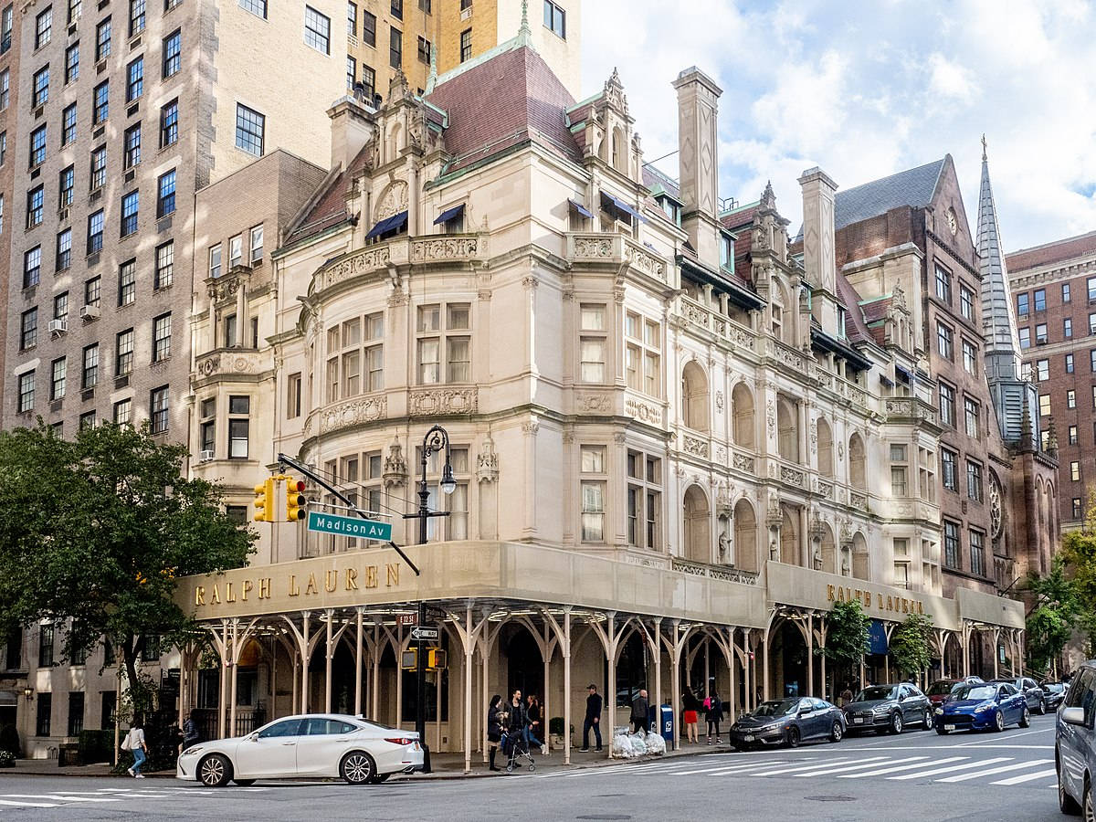 Ralph Lauren 建築 壁紙 — 大型裝飾米色建築，帶有拱形門廊和金色Ralph Lauren標牌，聳立在繁忙的城市街角，天空部分多雲。