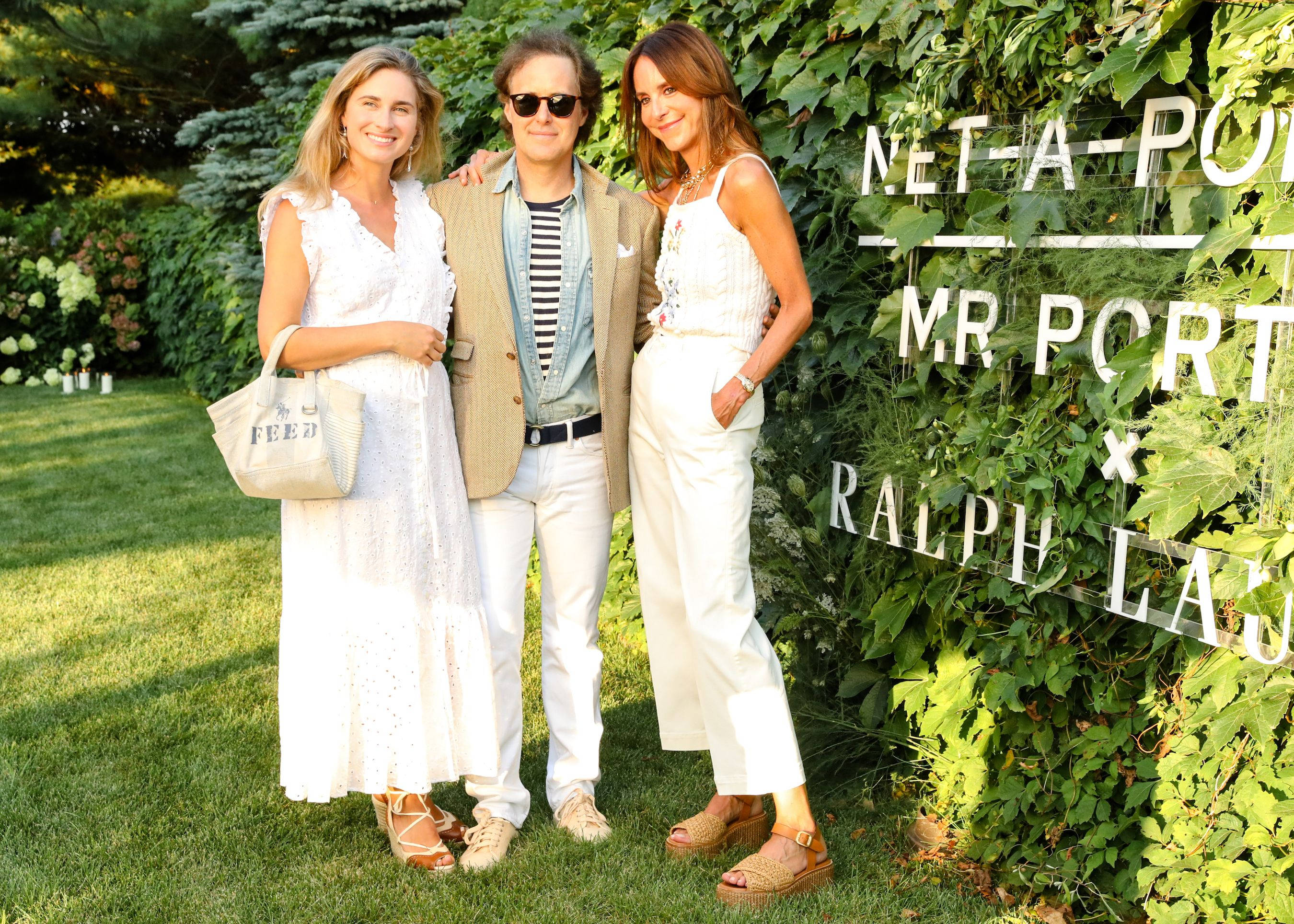 Ralph Lauren 派對 壁紙 — 三位穿著時尚的人士在陽光明媚的草坪上，旁邊是帶有白色文字品牌的茂密綠色牆壁，一起擺姿勢。