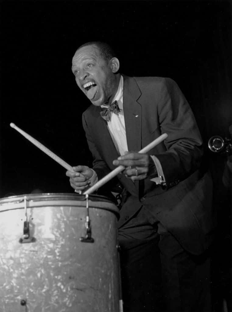 Ralph Nader 與 Lionel Hampton 共度時光 壁紙 — 一位身穿西裝和蝴蝶結的快樂爵士鼓手，在黑白照片中手持鼓棒放在低音鼓上，狂野大笑。