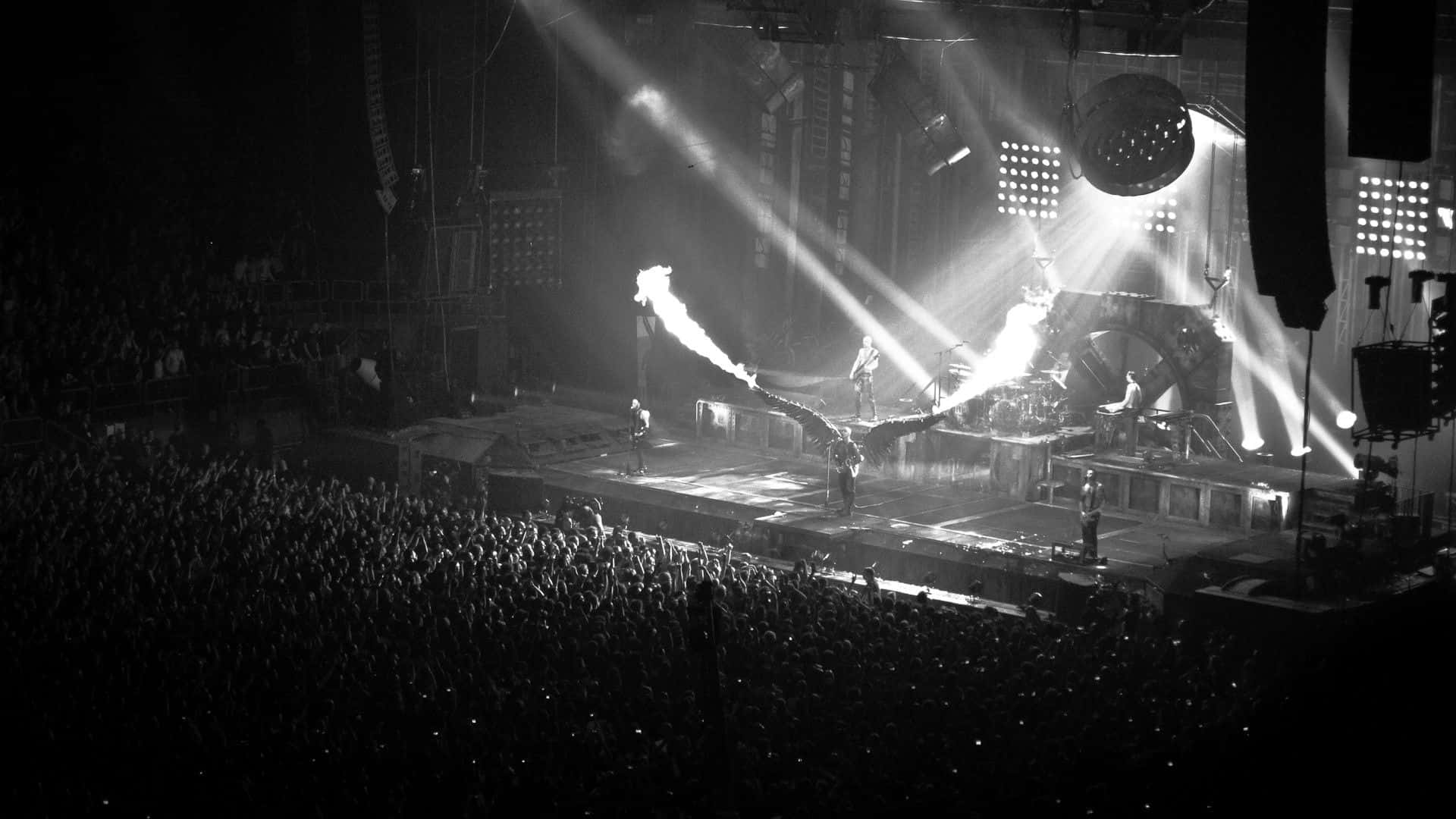 Rammstein 重金屬演唱會舞台背景 壁紙 — 黑白演唱會場景，舞台上嘅音樂家被戲劇性嘅聚光燈同煙霧籠罩，面對住一片剪影粉絲嘅海洋。