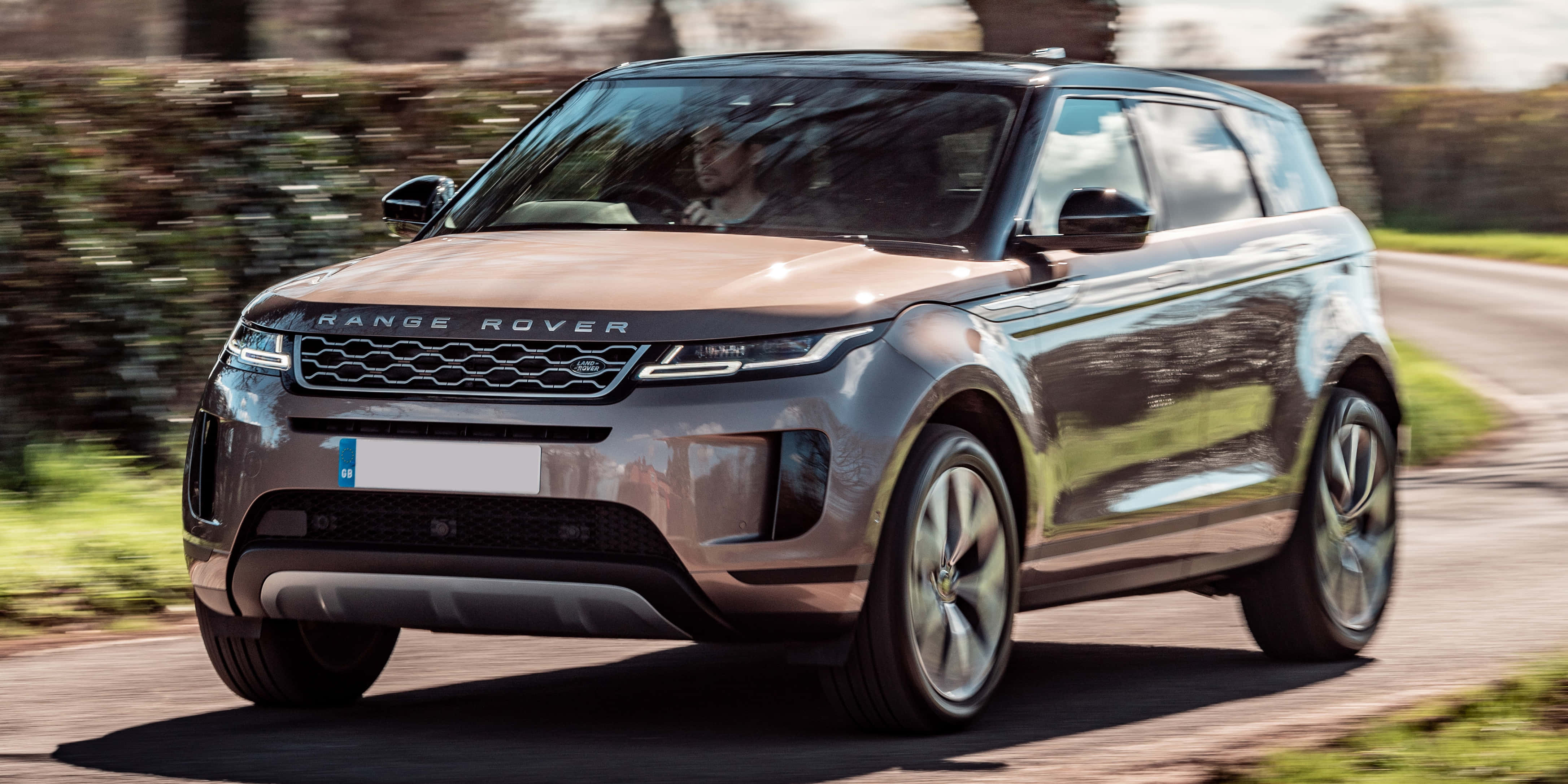 Range Rover 隨處可去 壁紙 — 一輛時尚的銀色Range Rover Evoque在陽光明媚的鄉村道路上疾馳，背景的綠色植物呈現動態模糊。