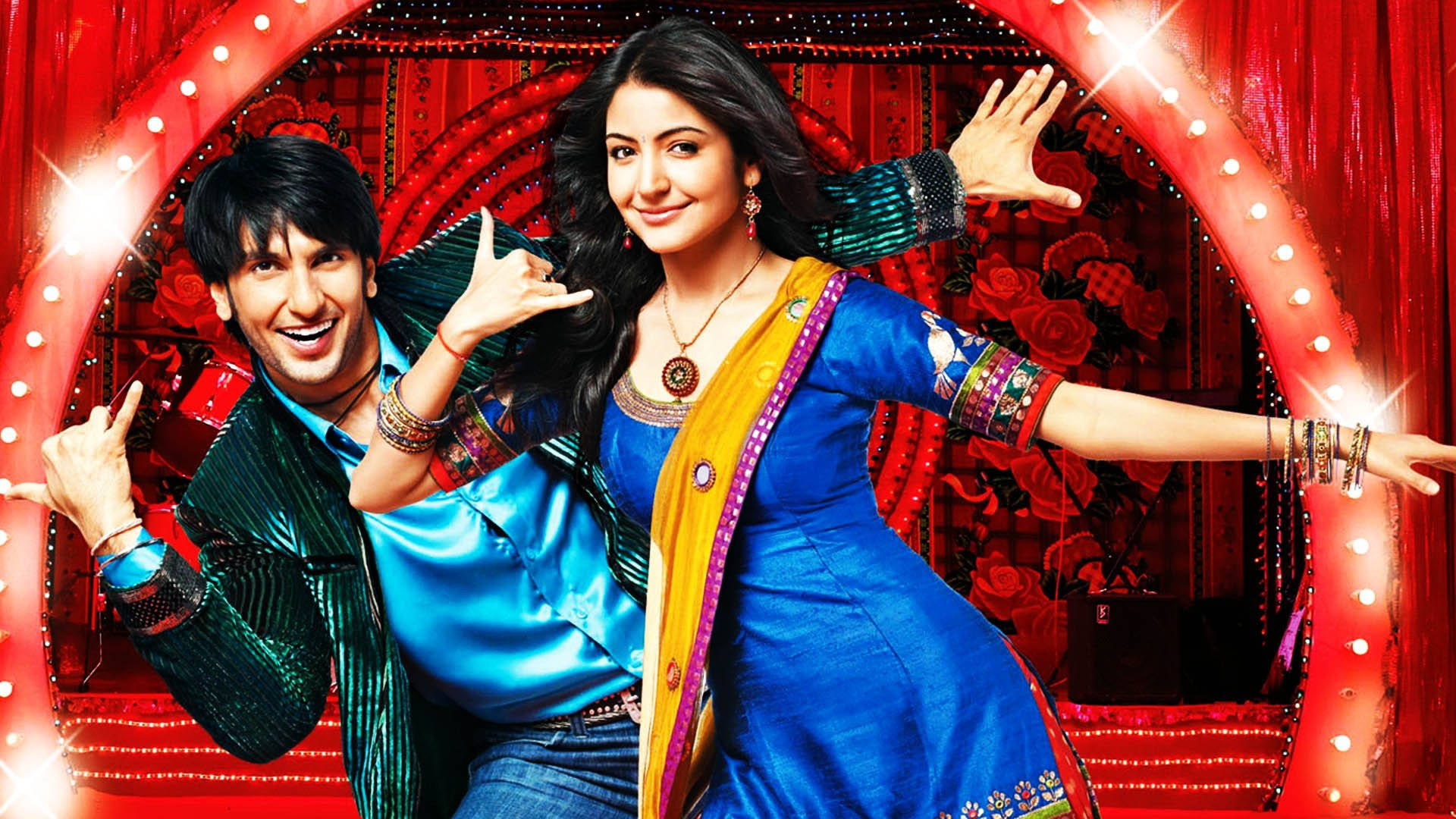 Ranveer Singh 在《Band Baaja Baaraat》電影中 壁紙 — 兩位歡樂的寶萊塢演員在明亮的舞台燈光下，以紅色花卉背景襯托，擺出俏皮的姿勢。