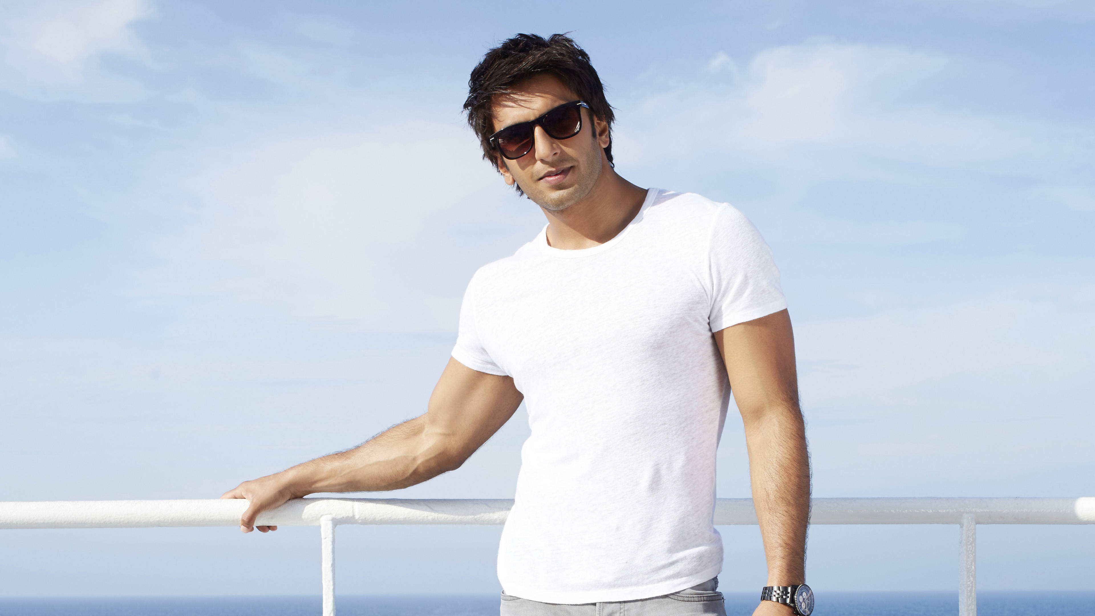 Ranveer Singh 在《Dil Dhadakne Do》電影中 壁紙 — 一位時尚男士戴著太陽眼鏡，隨意地靠在白色欄杆上，俯瞰著蔚藍天空下的海洋。