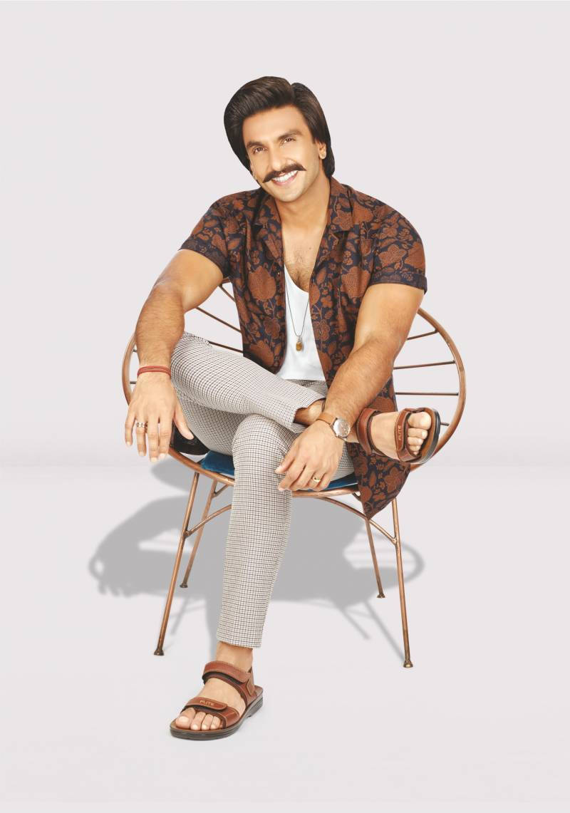 Ranveer Singh 為 Flite Footwear 品牌代言 壁紙 — 一位留鬍鬚的男士微笑著，隨意地坐在鐵絲椅上，穿著圖案棕色襯衫和格子褲。