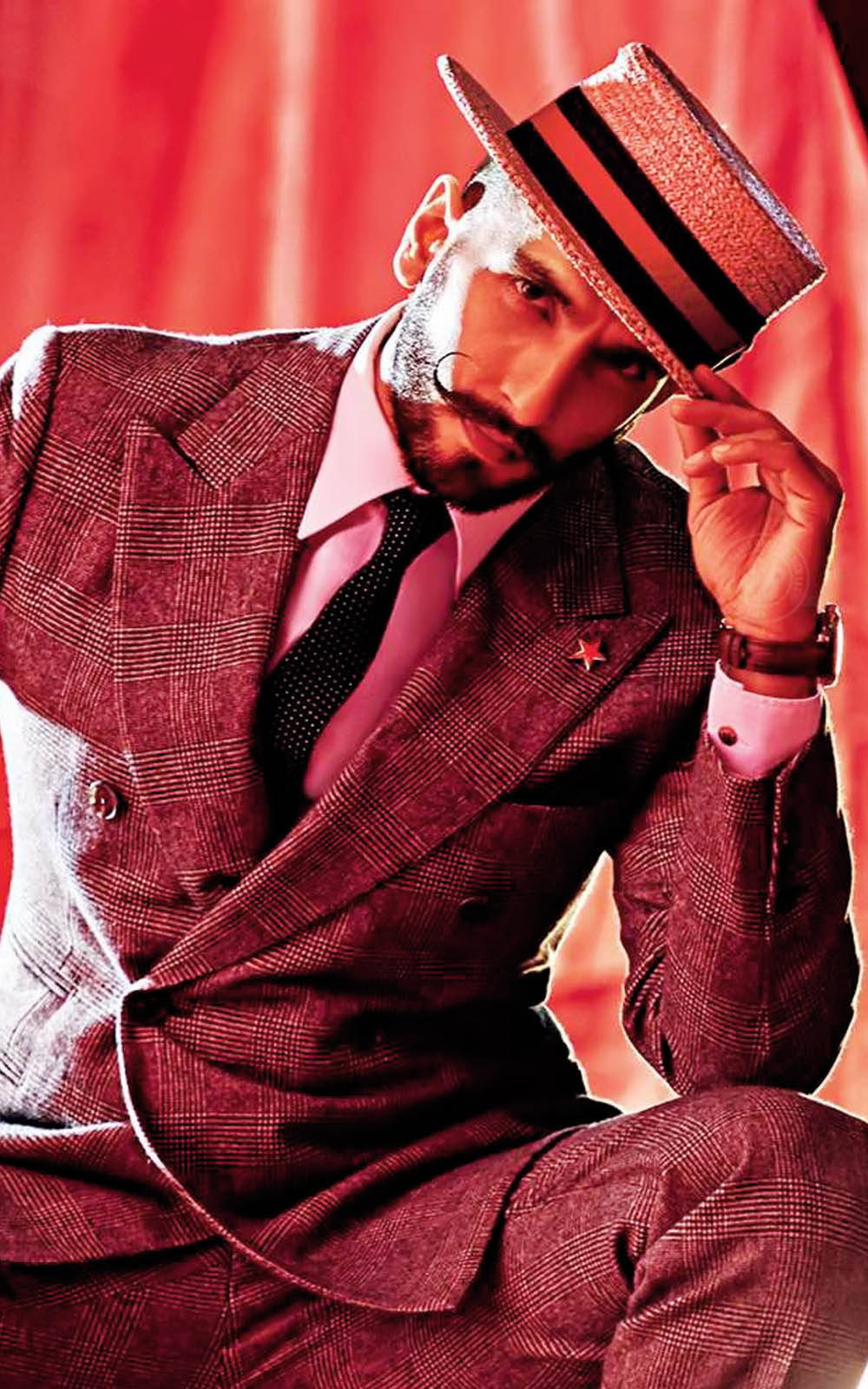 Ranveer Singh 為《GQ India》拍攝時裝照 壁紙 — 一位衣著講究、身穿格紋西裝和條紋帽子的男士，在鮮紅色的窗簾背景下自信地擺姿勢。