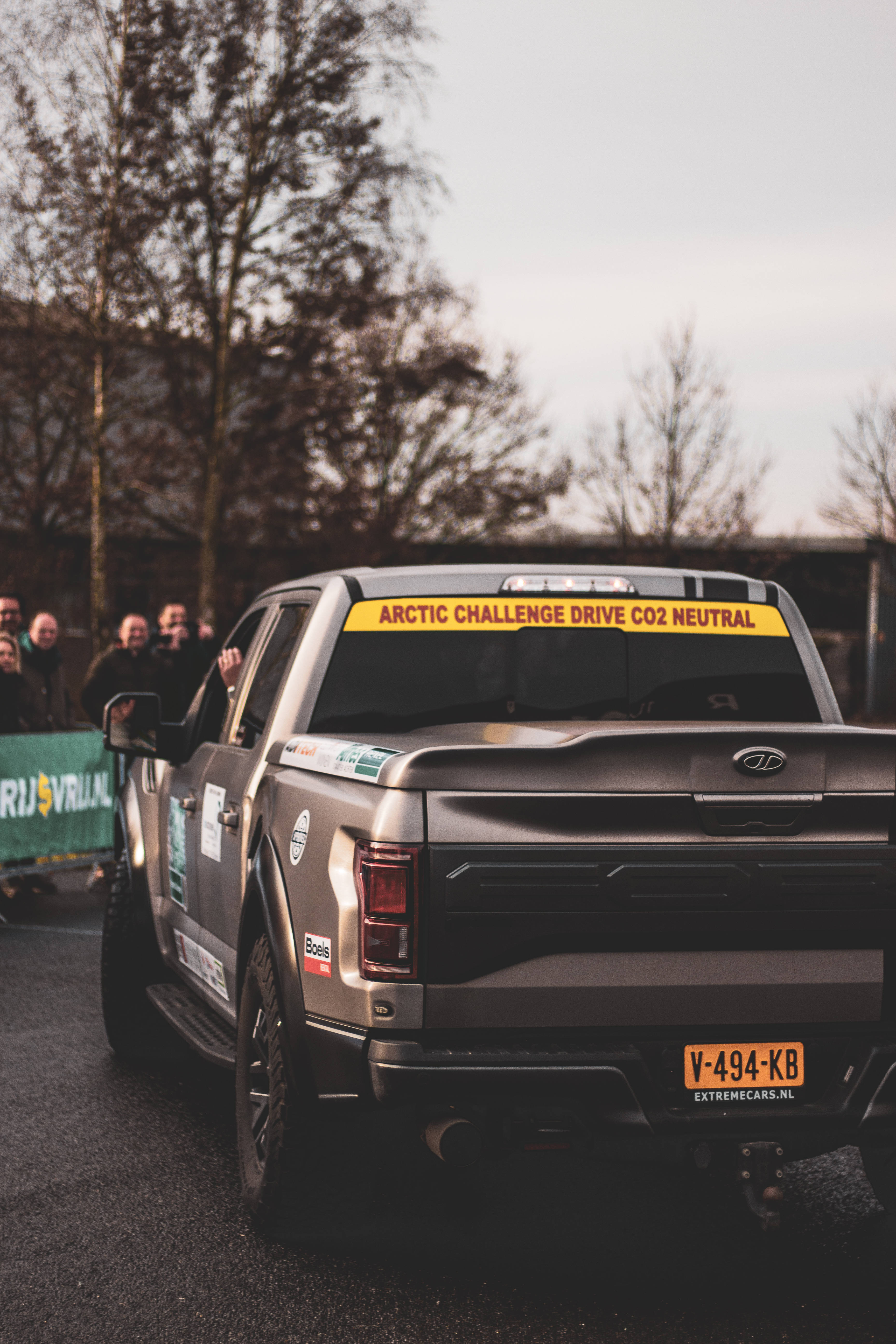 福特Raptor皮卡 壁紙 — 一輛銀色皮卡車帶有'Arctic Challenge Drive CO2 Neutral'貼紙，在黃昏時駛過觀眾。