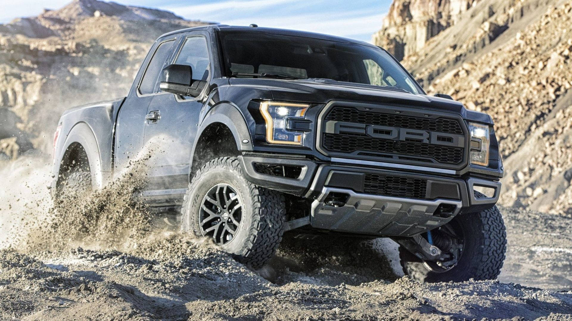 福特Raptor越野駕駛 壁紙 — 一輛黑色福特 F-150 Raptor 卡車在明亮的日光下，在崎嶇的泥濘地形上行駛，揚起泥漿和灰塵。