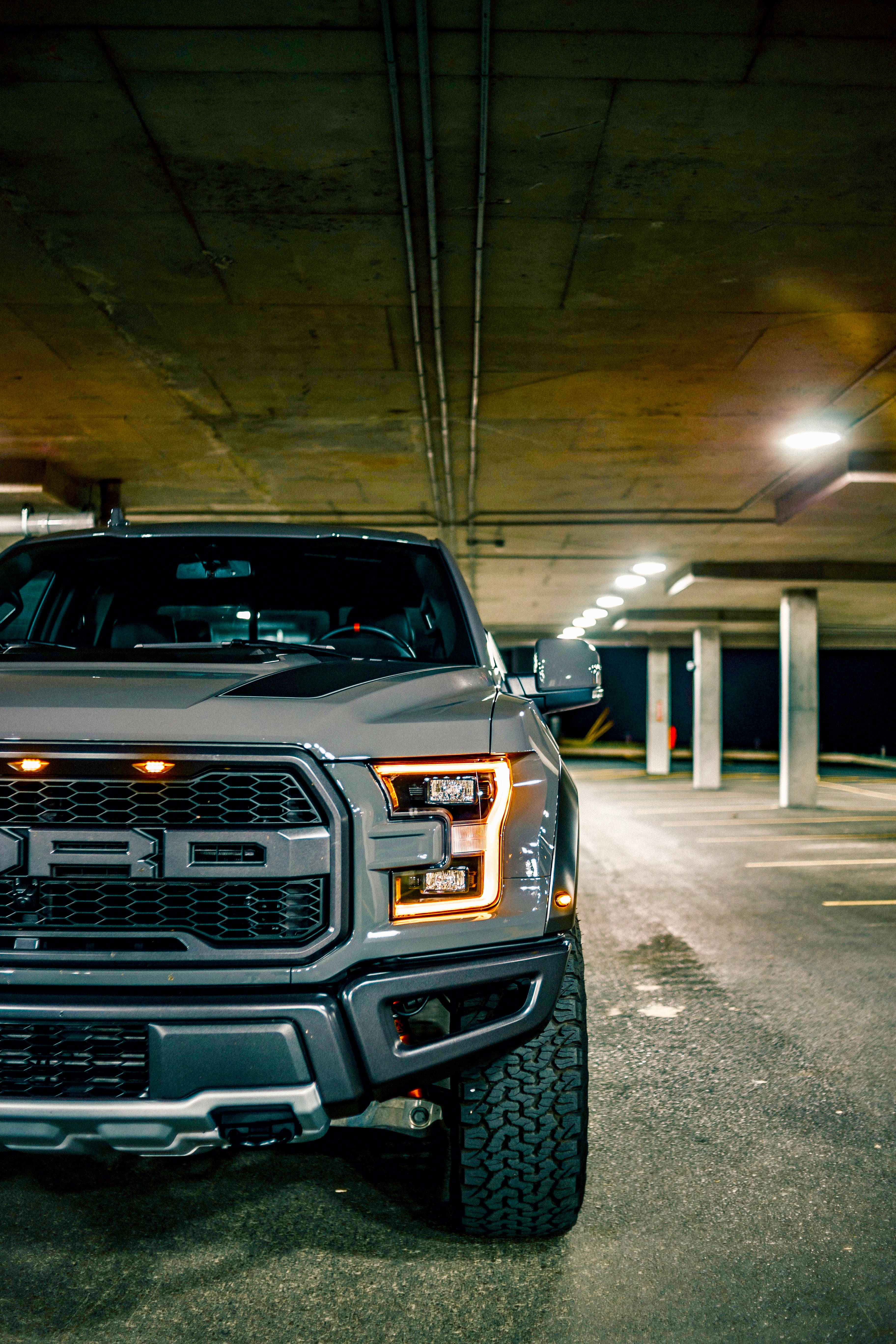 福特Raptor橙色LED頭燈 壁紙 — 一輛灰色福特F-150猛禽卡車，閃爍琥珀色車頭燈，主宰著昏暗的地下停車場。