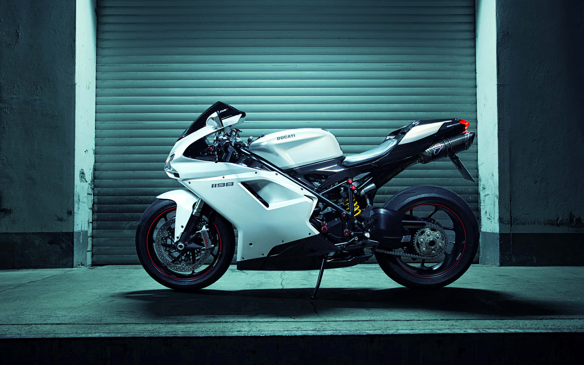 賽道-ready 超級摩托車 壁紙 — 一架時尚的白色Ducati 998電單車，在清涼的人造燈光下，停泊在青綠色金屬車庫門前。
