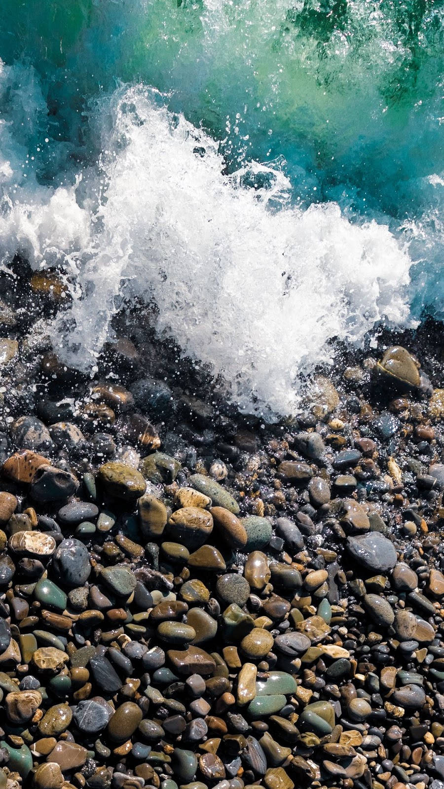 藍綠色海浪拍打陽光照耀的卵石海灘，帶有白色泡沫。
