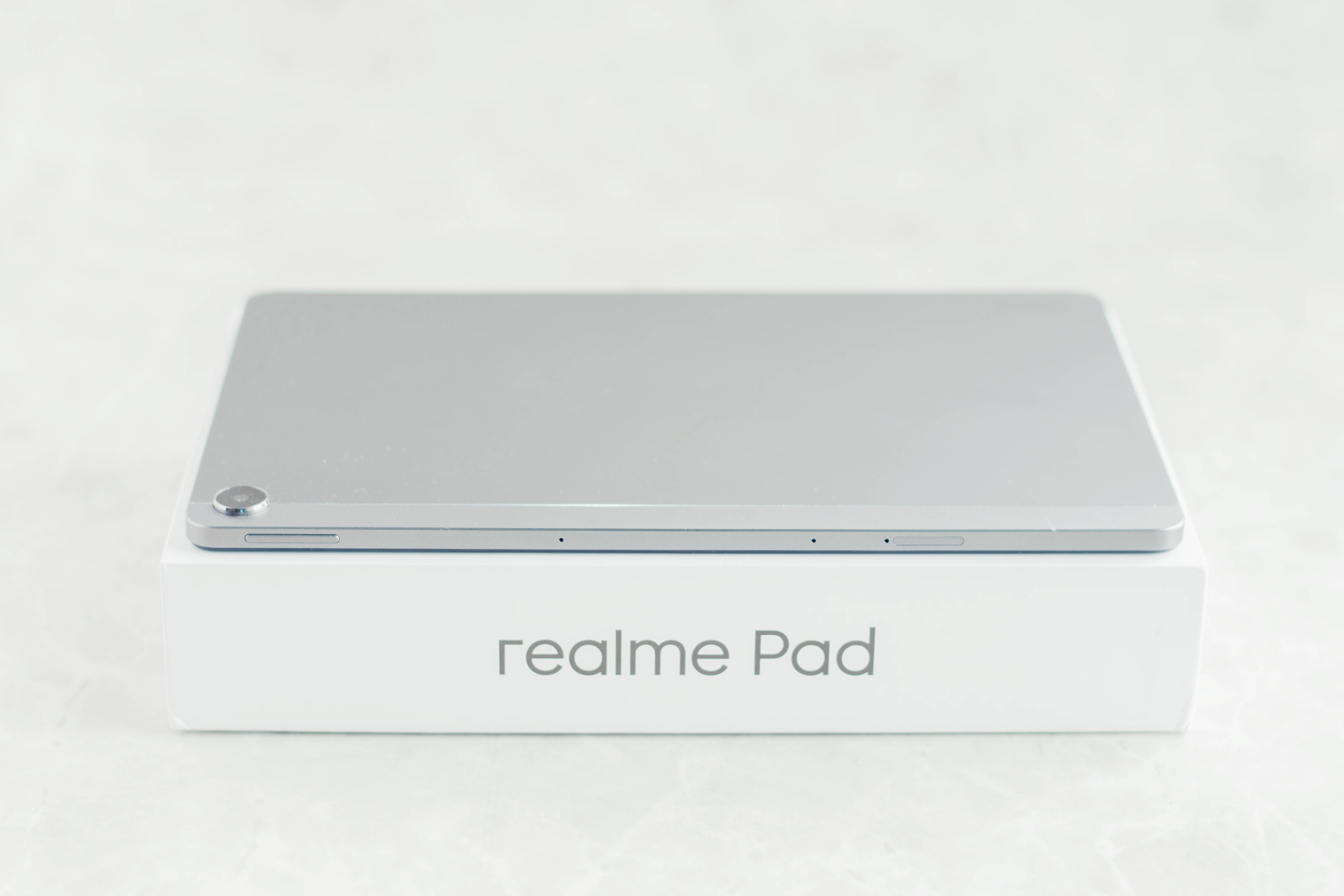Realme Pad 灰色款 壁紙 — 一部時尚的銀色 realme Pad 平板電腦放在其白色品牌盒子上，背景為柔軟的紋理。
