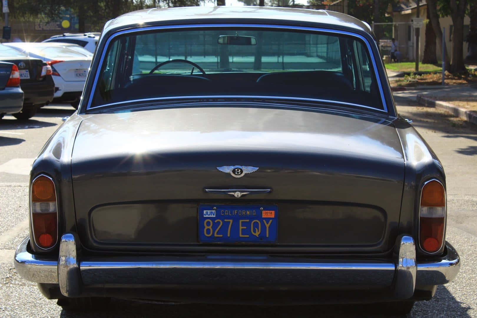 Bentley T1 桌布 壁紙 — 經典深灰色賓利，帶有鍍鉻飾條和加州車牌，停放在陽光明媚的街道上的後視圖。