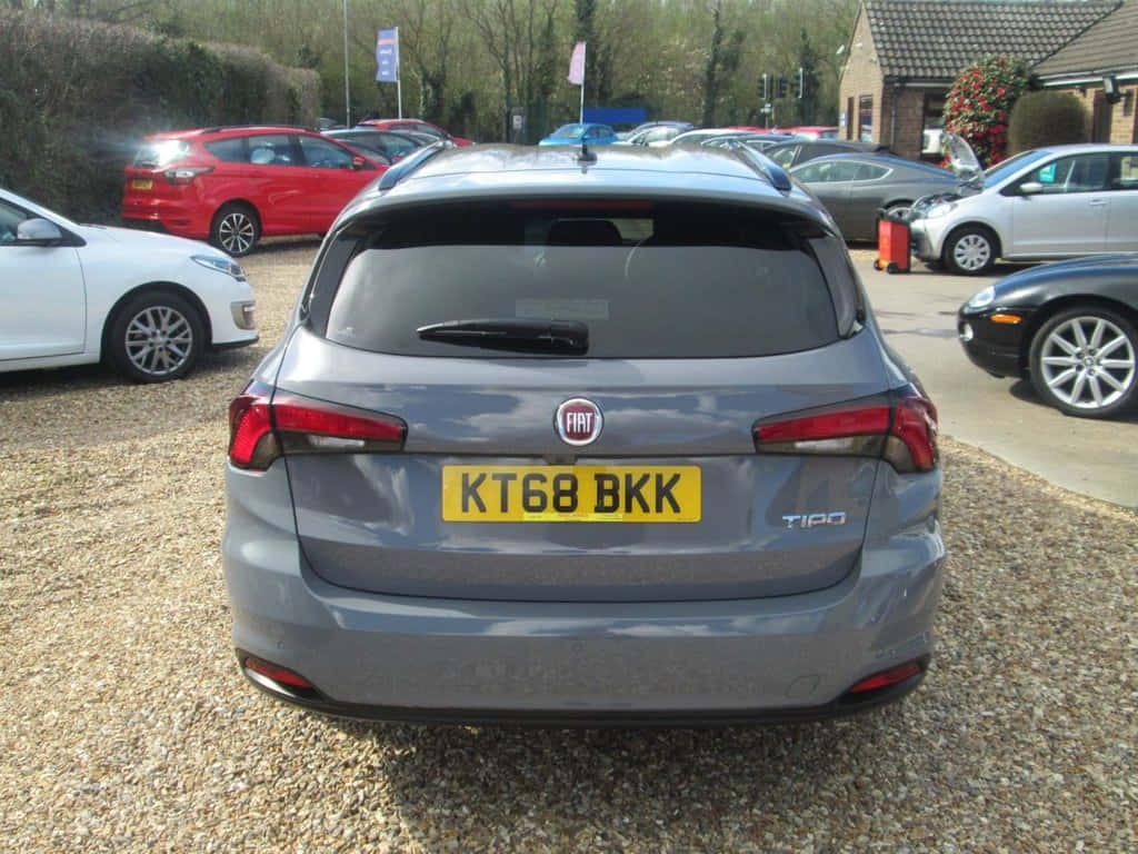 Fiat Tipo 桌布 壁紙 — 從後方觀看一輛灰色 Fiat Tipo 旅行車停泊在陽光普照的停車場碎石地上，附近有其他車輛。