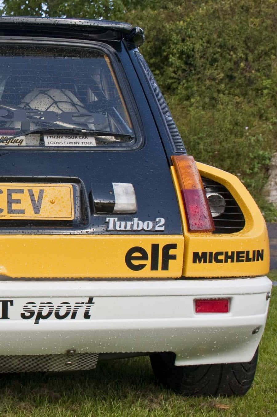 Renault 5 Turbo 桌布 壁紙 — 一輛復古藍黃色雷諾5 Turbo 2拉力賽車停在草地上，表面有雨滴的後視圖。
