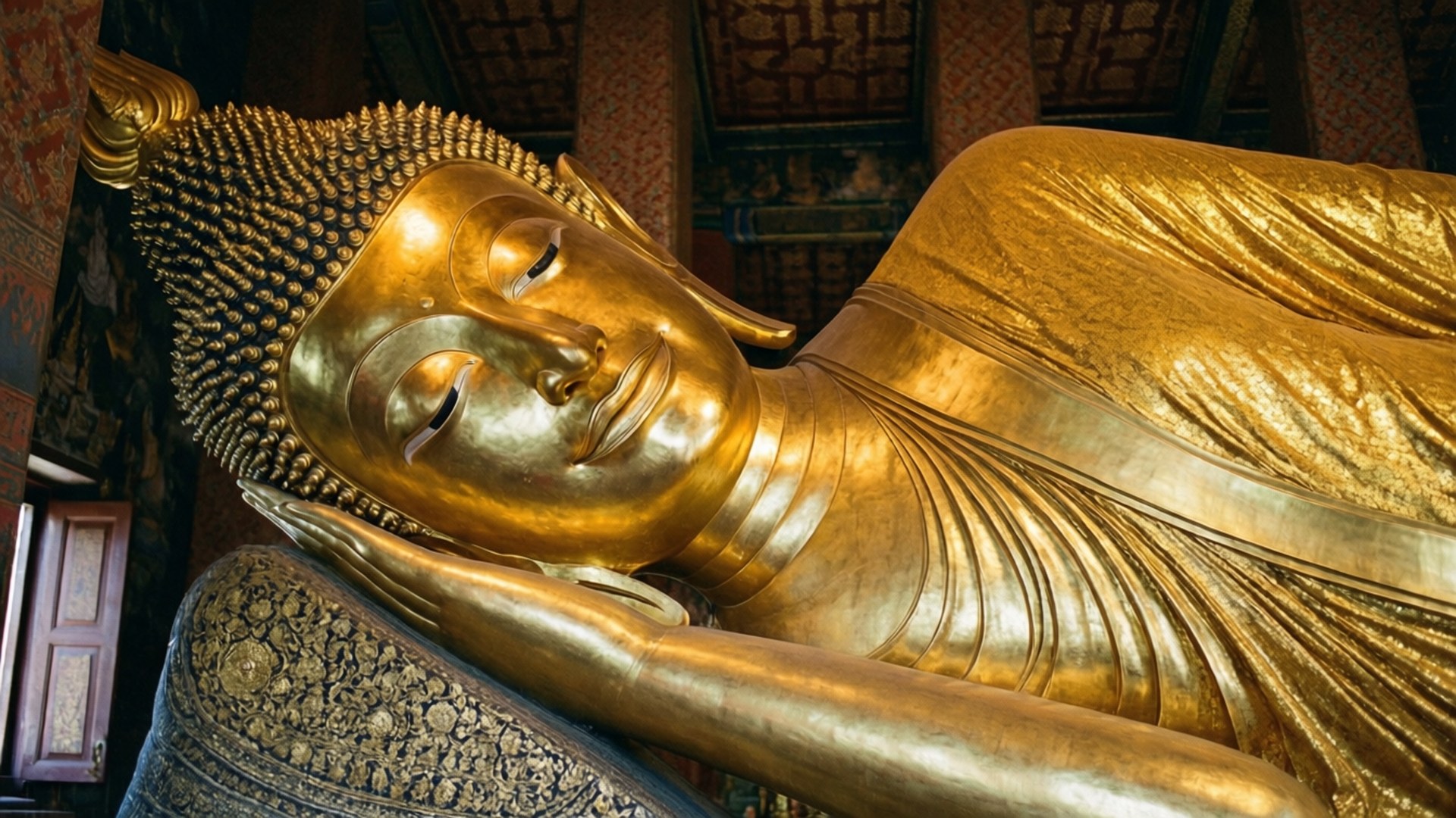 金色臥佛雕像在寺廟內精緻木樑下安詳地休息。