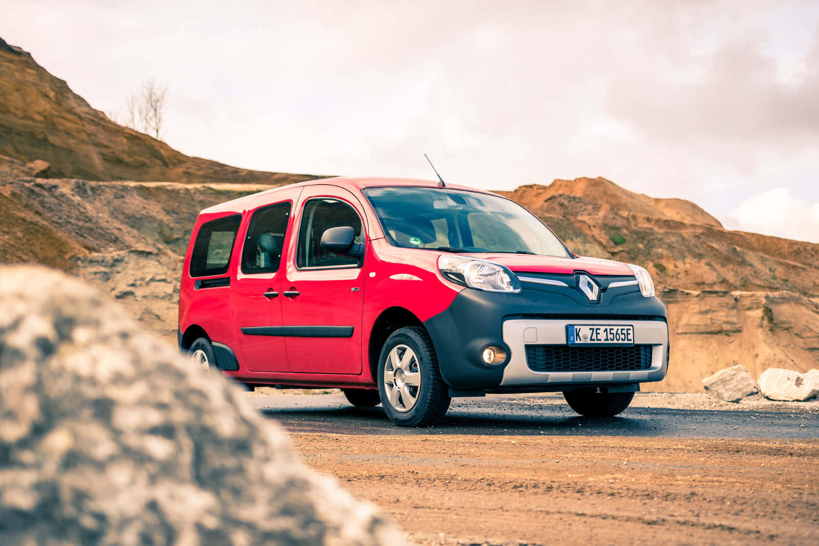Renault Kangoo 桌布 壁紙 — 一輛紅色和黑色的雷諾Kangoo客貨車停泊在碎石路上，背景是岩石丘陵，天空多雲。