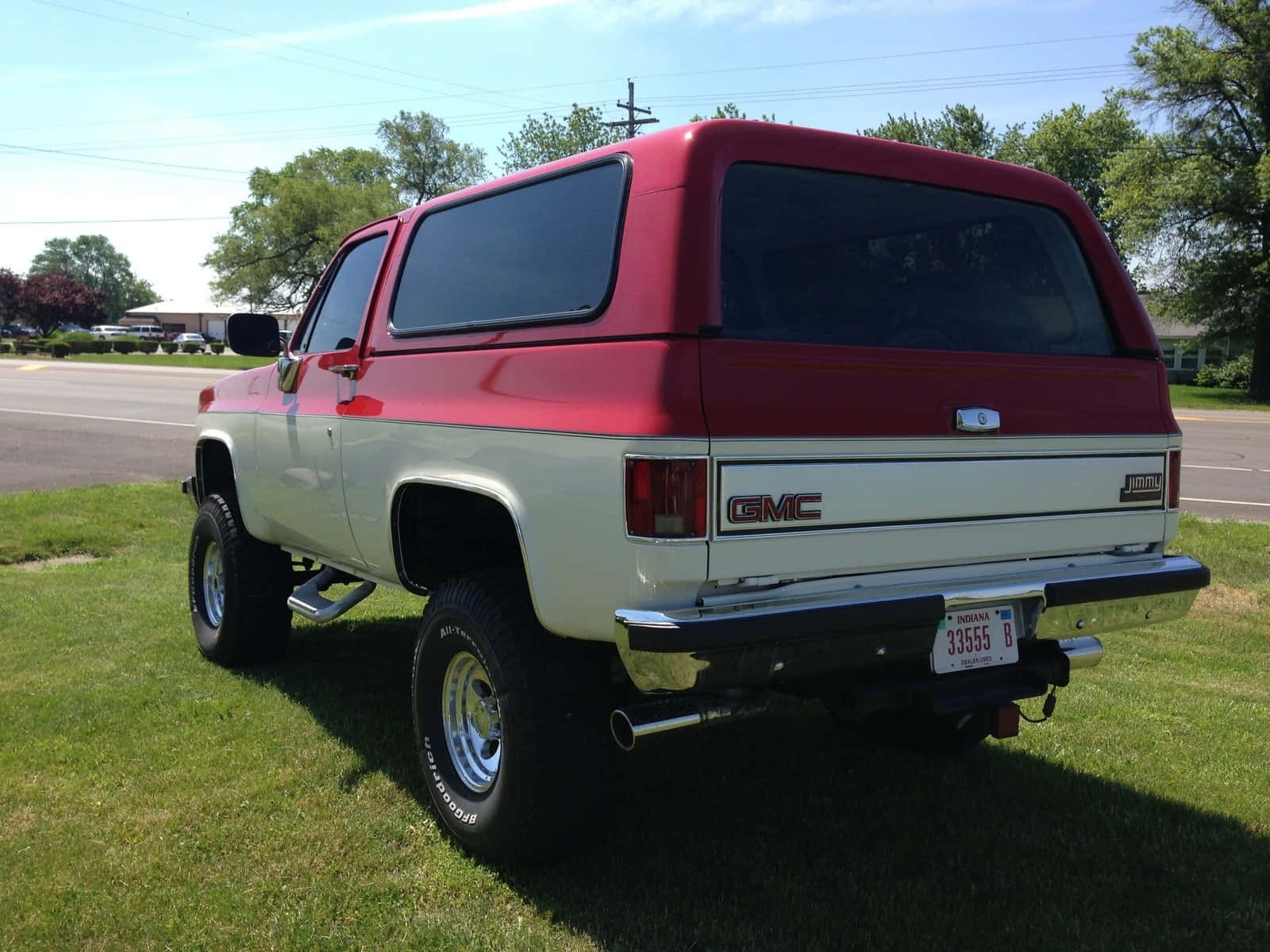 Gmc Jimmy 桌布 壁紙 — 一輛紅色和白色的升高GMC Jimmy SUV停泊在草地上，背景是晴朗的天空和樹木。
