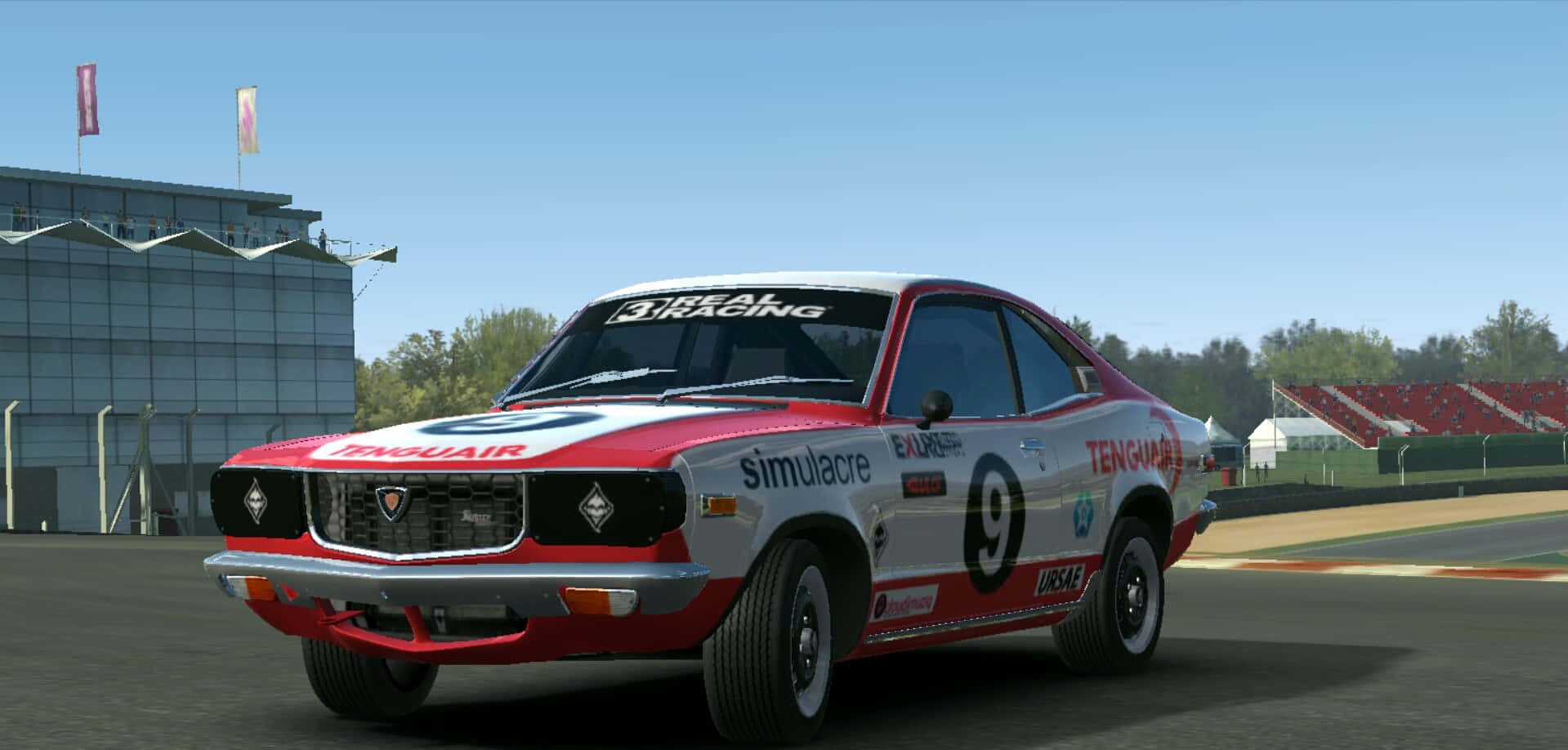 Mazda Rx-3 桌布 壁紙 — 一架紅白相間、編號九的復古賽車在陽光明媚的賽道上飛馳，旁邊是看台和一座現代建築。