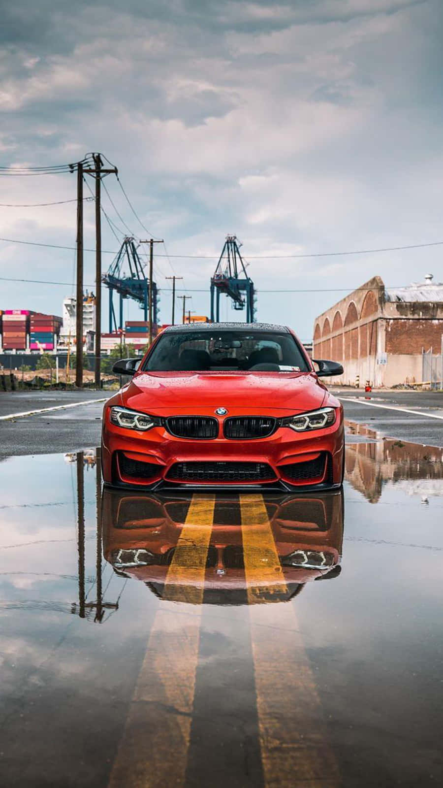 紅色BMW汽車倒映在潮濕工業街道的水坑中。