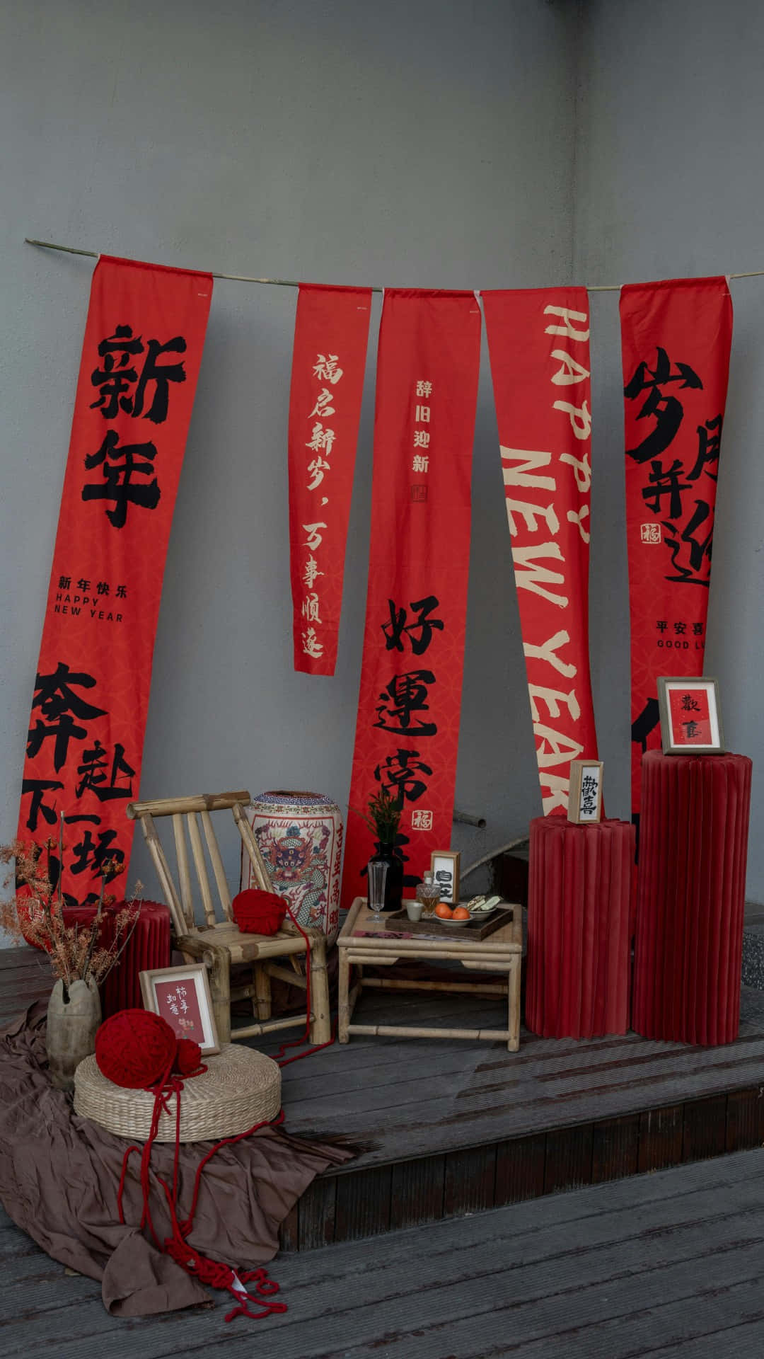  壁紙 — 紅色中國新年書法橫幅掛在竹椅和桌子上方，木質甲板上裝飾著節日紅色裝飾。