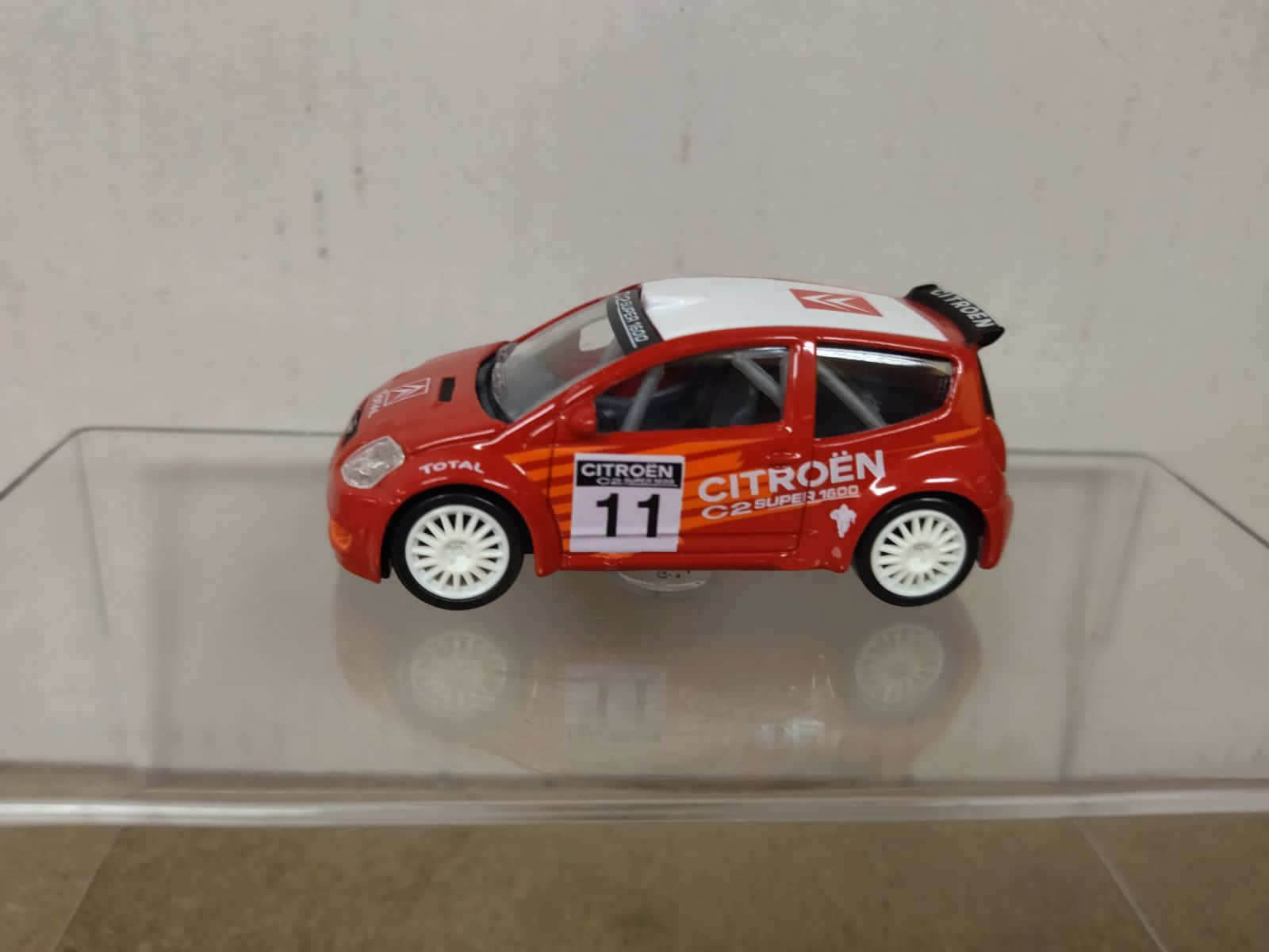 Citroen C2 Super 1600 桌布 壁紙 — 一輛紅色雪鐵龍C2拉力賽車模型，編號11，放置在透明展示架上，反射出其光澤表面。