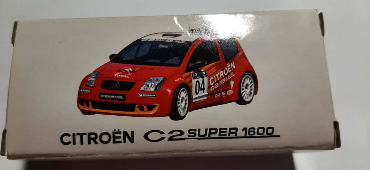 Citroen C2 Super 1600 桌布 壁紙 — 一個紅色雪鐵龍C2 Super 1600拉力賽車模型盒，帶有白色賽車貼紙和號碼04，背景為純白色。