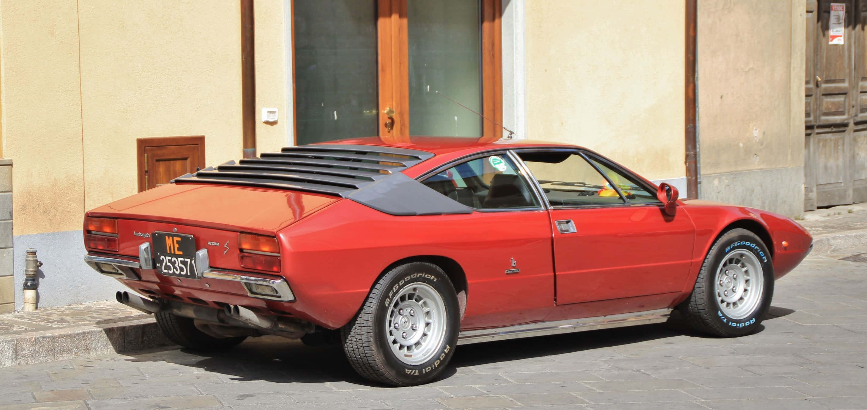 Lamborghini Urraco 桌布 壁紙 — 一輛鮮紅色經典法拉利308 GTB停泊在陽光普照的鵝卵石街道上，旁邊是一棟米色建築。