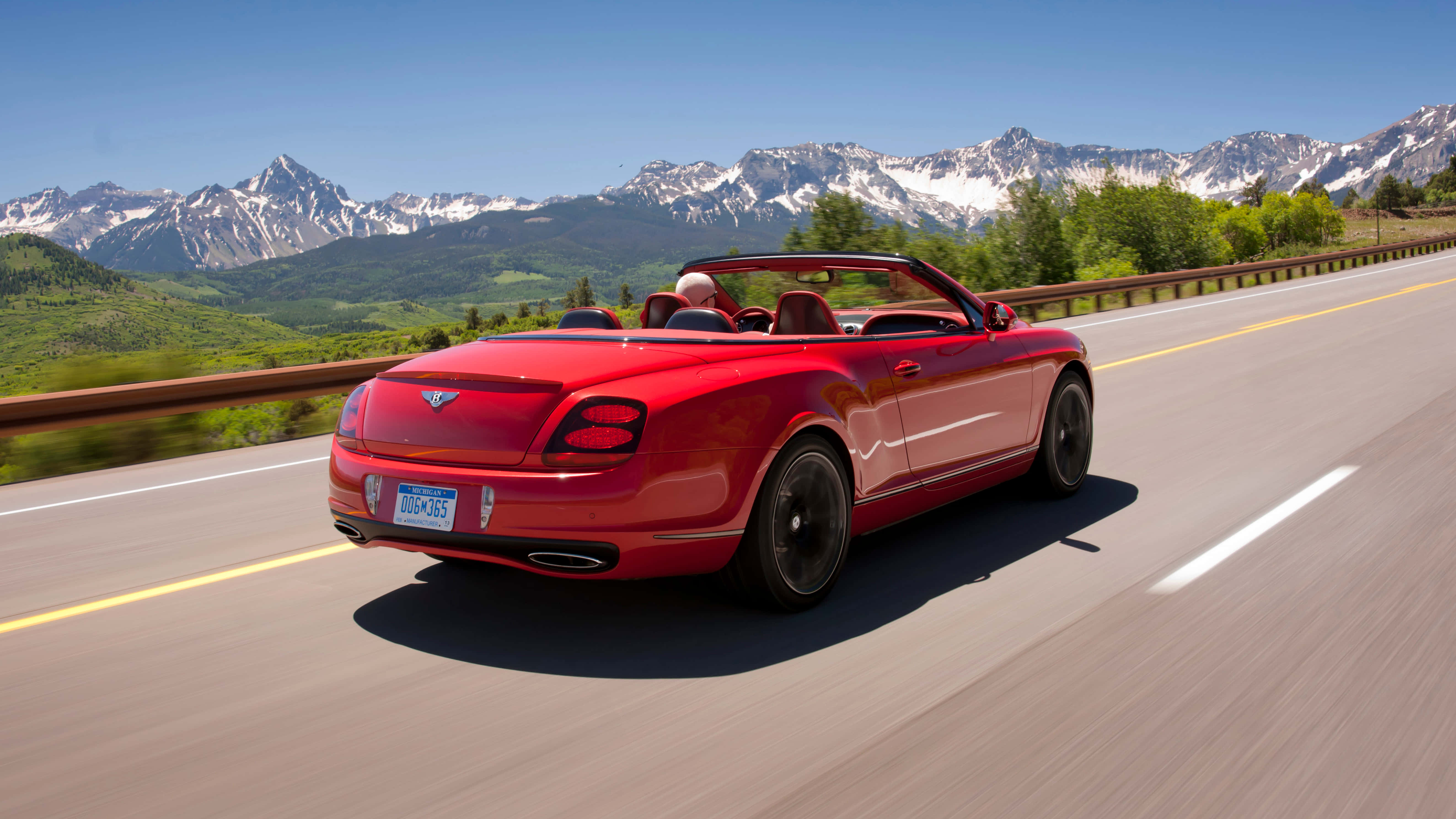 Bentley Continental Supersports 桌布 壁紙 — 一輛紅色敞篷跑車在雪山頂和綠色山谷之間的山區高速公路上行駛，天空湛藍清澈。