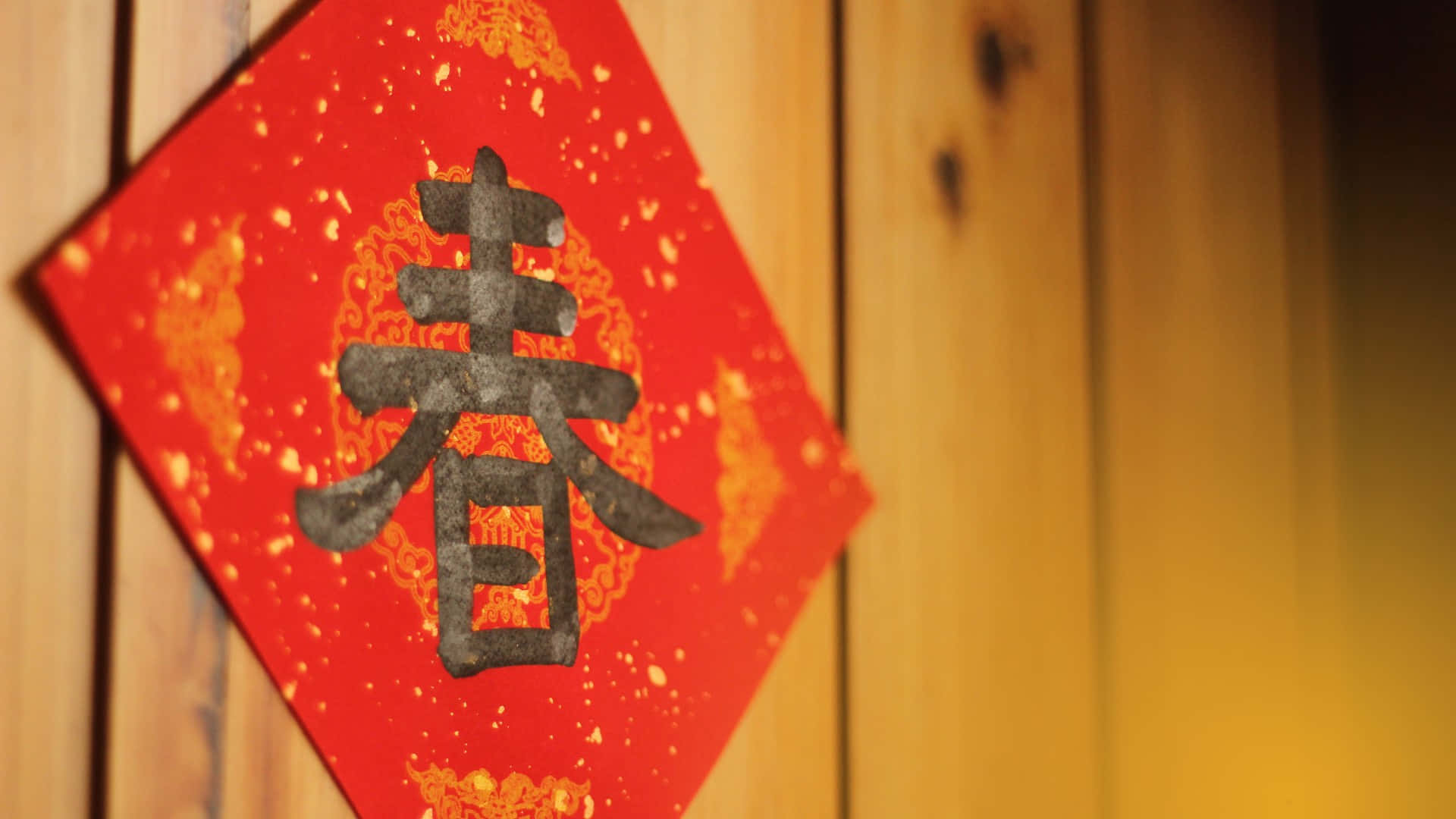  壁紙 — 一個紅色菱形嘅中國新年裝飾，上面有「春」字，掛喺溫暖嘅木板上。