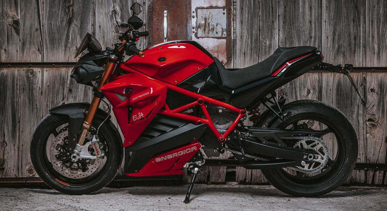  壁紙 — 一架搶眼的紅色Energica EVA電動電單車，停泊在風化的木製穀倉門前。