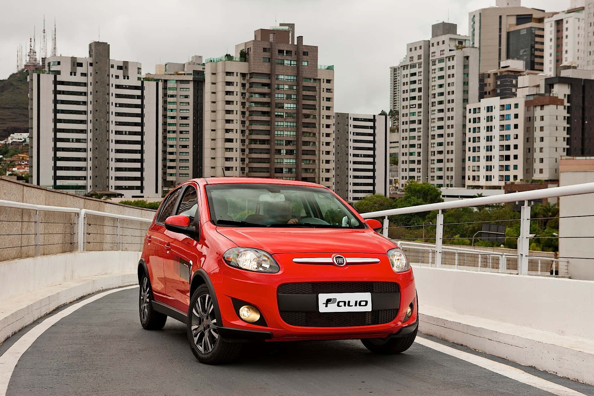 Fiat Palio 桌布 壁紙 — 一輛鮮紅色的Fiat Palio在彎曲的城市高架橋上行駛，陰沉的背景中現代高樓大廈聳立。